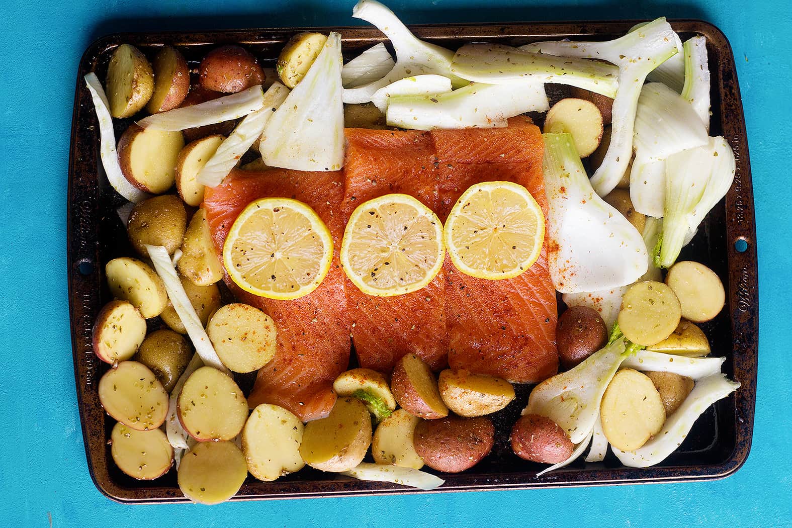 To make baked salmon fillet, mix all the spices with lemon and olive oil and brush them on salmon fillet. Spread the veggies around and bake. 