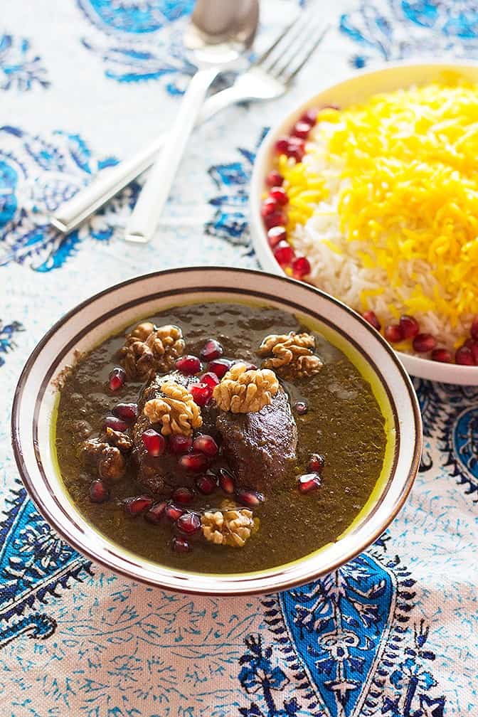 A bowl of fesenjan topped with walnuts and pomegranate. 