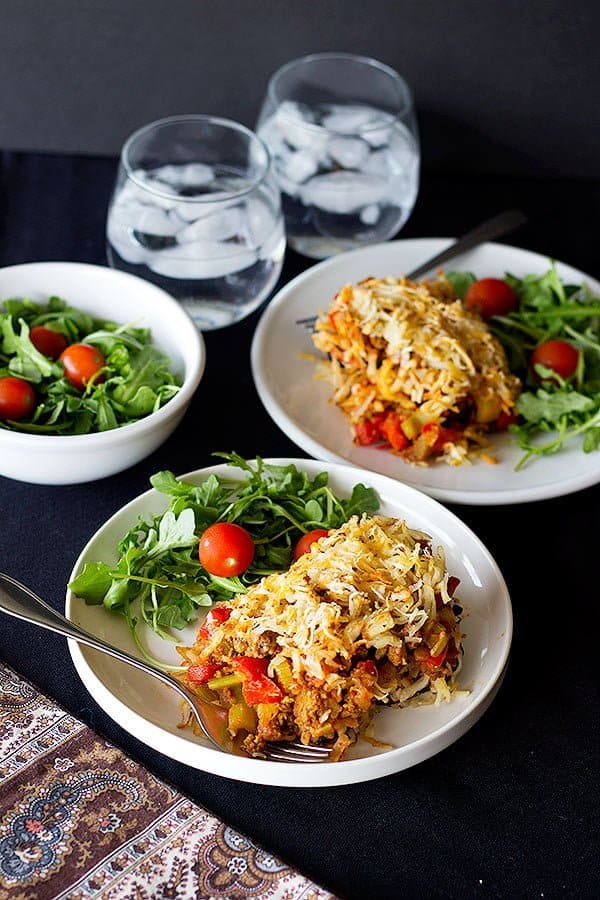 two plates of eggplant casserole with arugula and tomatoes. 