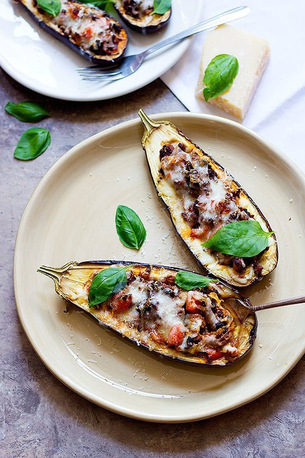 Overhead view of stuffed eggplant parm arranged with basil and a block of parmesan cheese