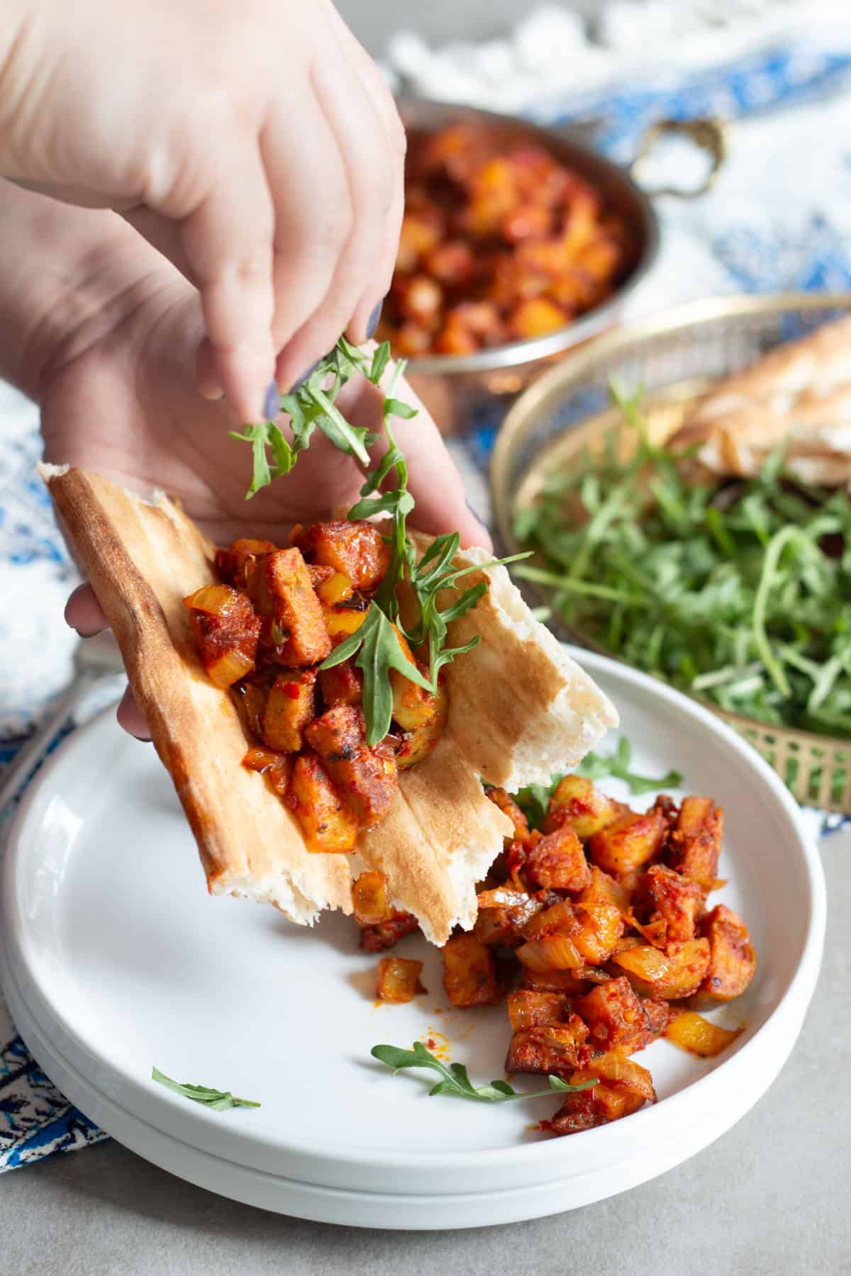 a shot of a woman rolling up cooked sausage and potatoes with arugula