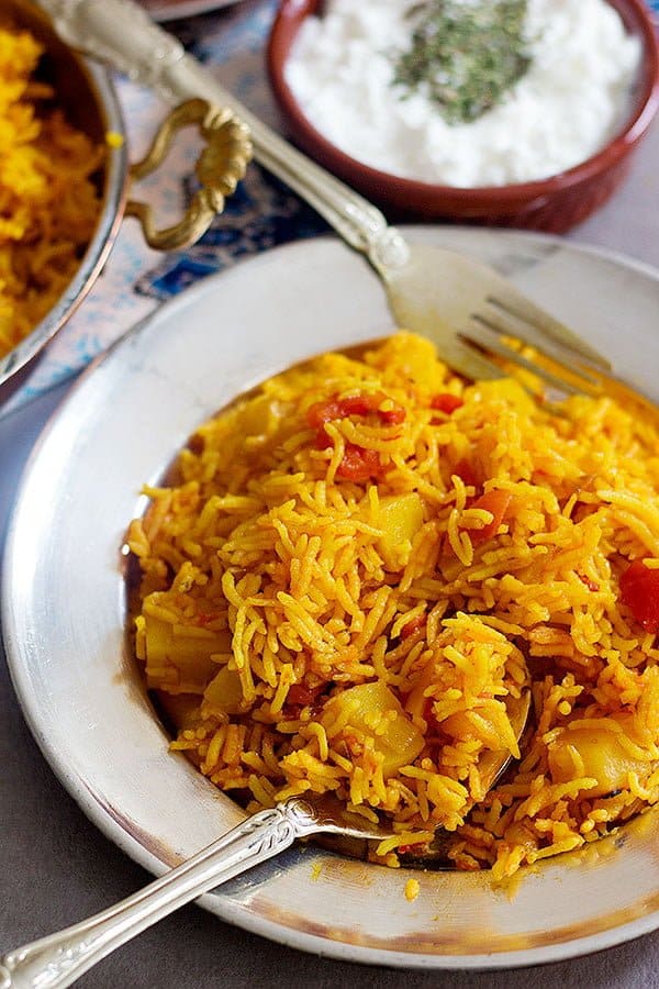 A plate of Persian style tomato rice with yogurt on the side. 