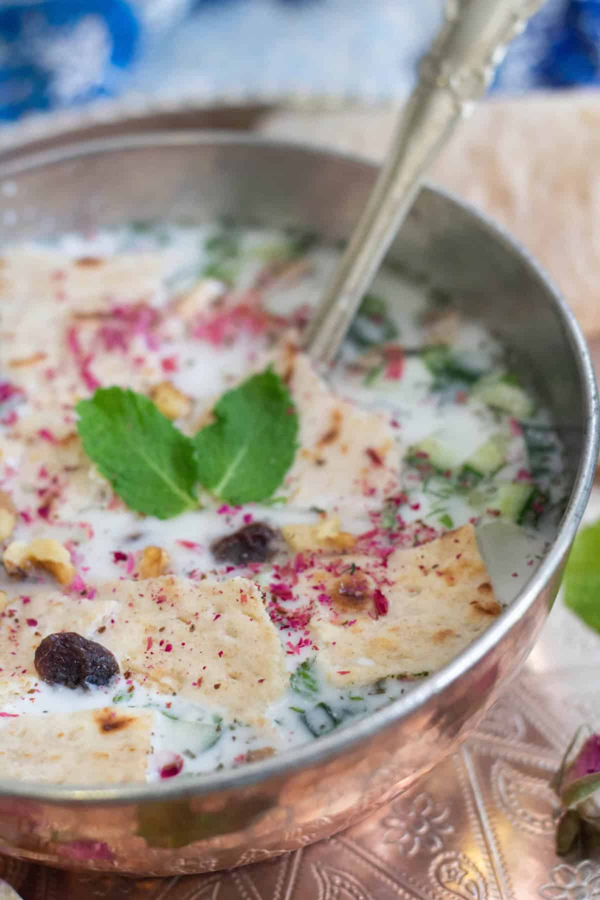 A bowl of Persian cold yogurt soup on a blue backdrop. 