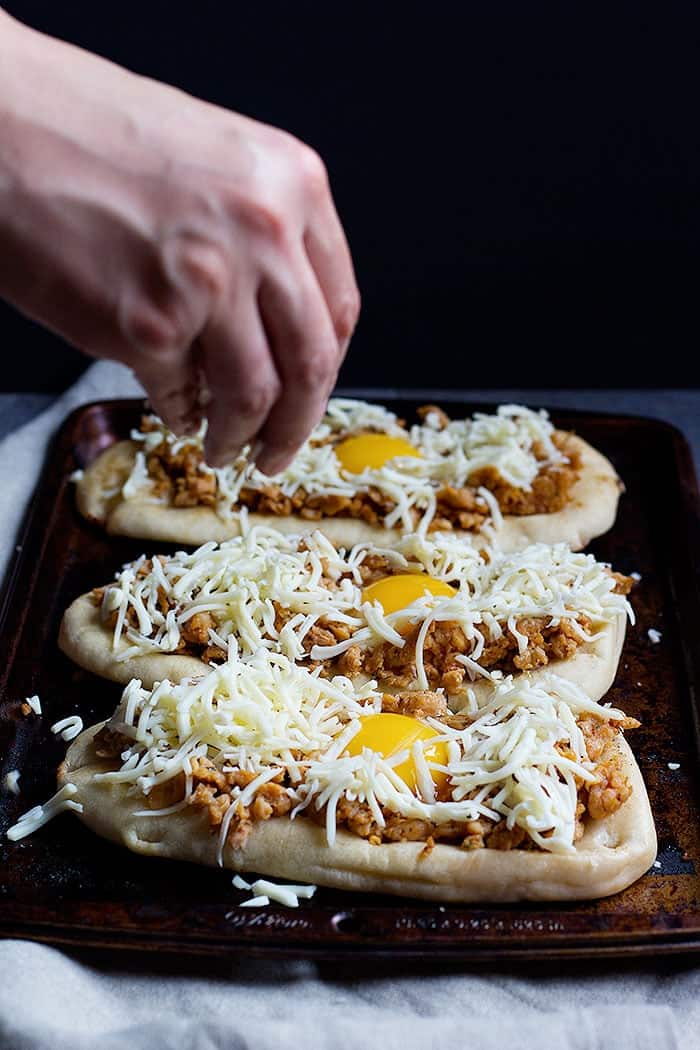 Top breakfast pizzas with sausage and shredded mozzarella cheese.