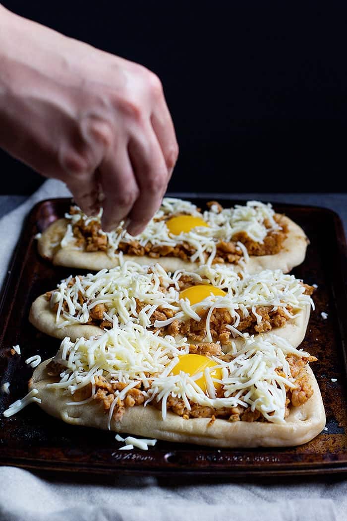 Top breakfast pizzas with sausage and shredded mozzarella cheese. 