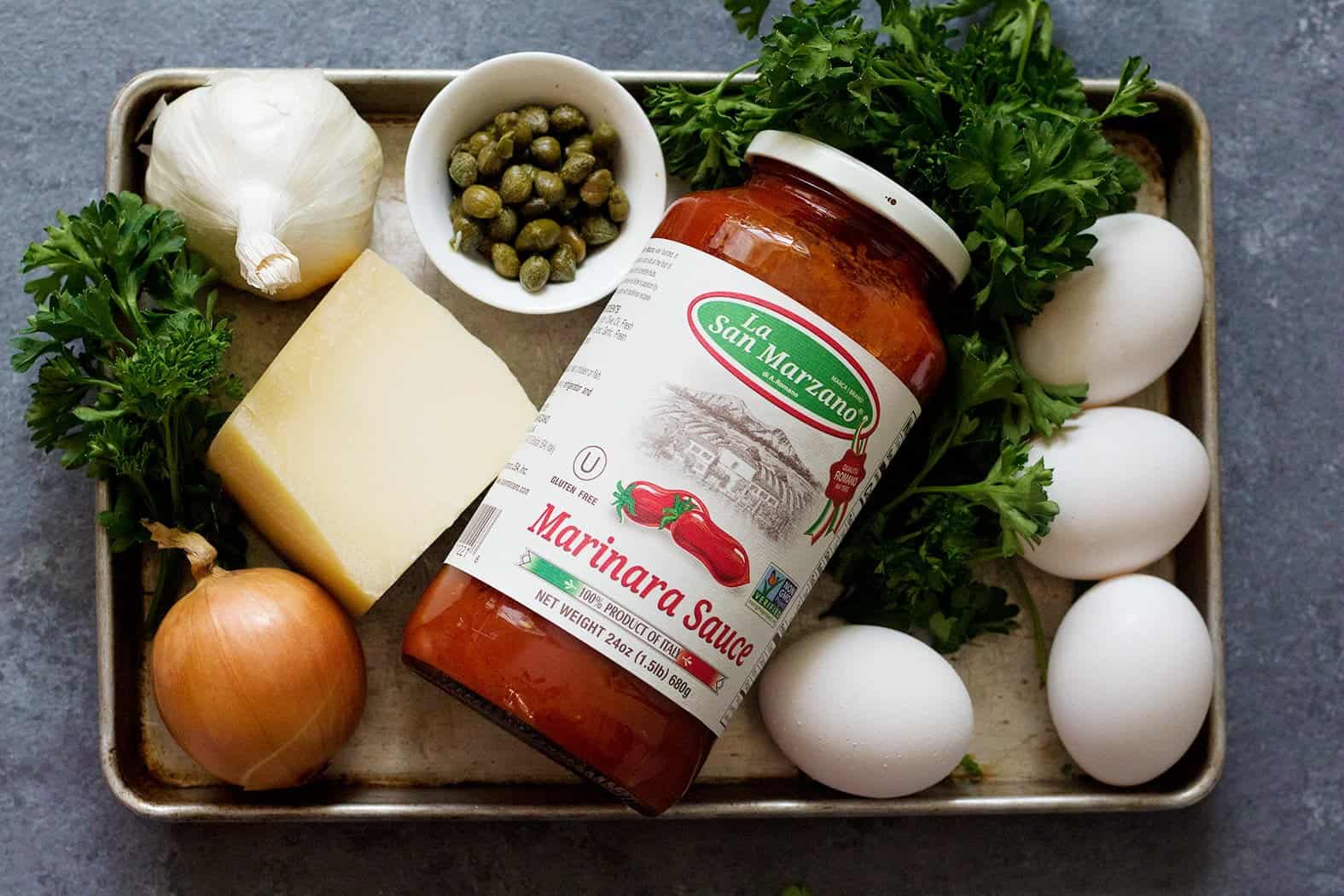 Ingredients to make baked eggs: onions, bell pepper, eggs, La San Marzano Marinara sauce, capers, eggs, parmesan and mozzarella cheese.