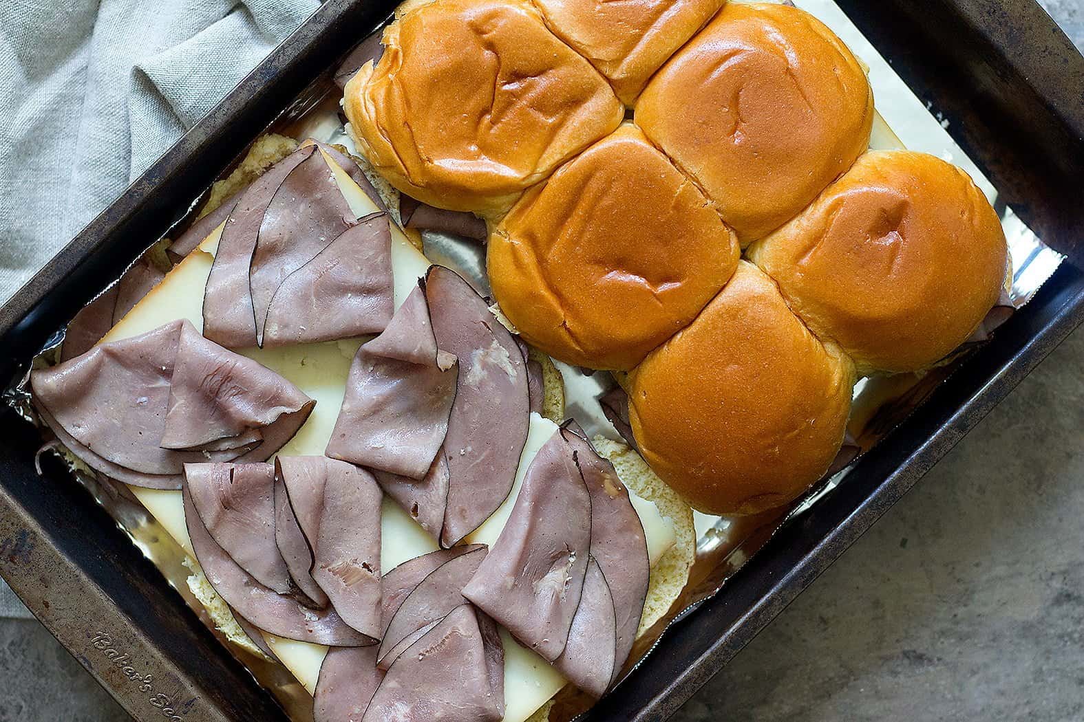 Place the bottoms in a 9x13 baking pan or on a baking sheet lined with aluminum foil. Spread a little bit of the melted butter mixture on the rolls. Top with half of the roast beef and then top with cheese. Add another layer of roast beef and finish with the top layer of the Hawaiian rolls. 