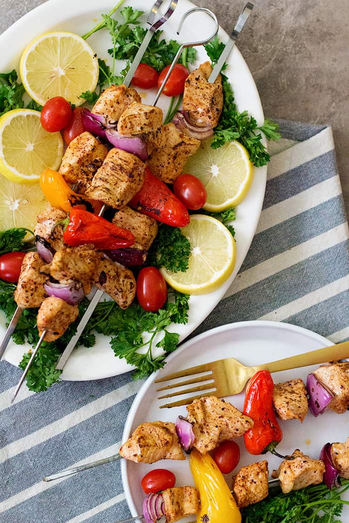 grilled chicken shish kabob on a plate with lemon and tomatoes. 