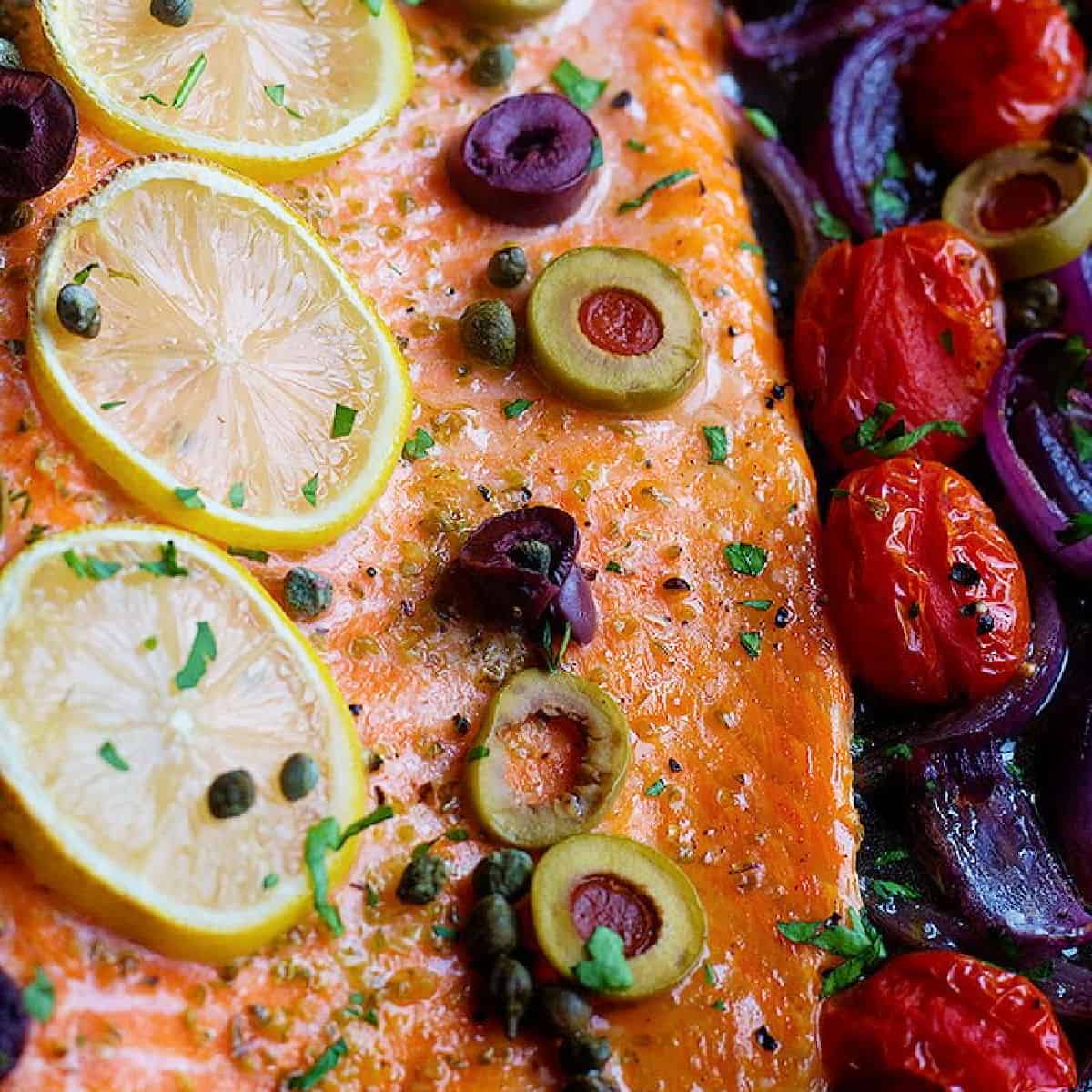 The best ever oven baked salmon is here! Flaky and moist Alaska salmon with olives and capers on a bed of vegetables is the best weeknight dinner!
