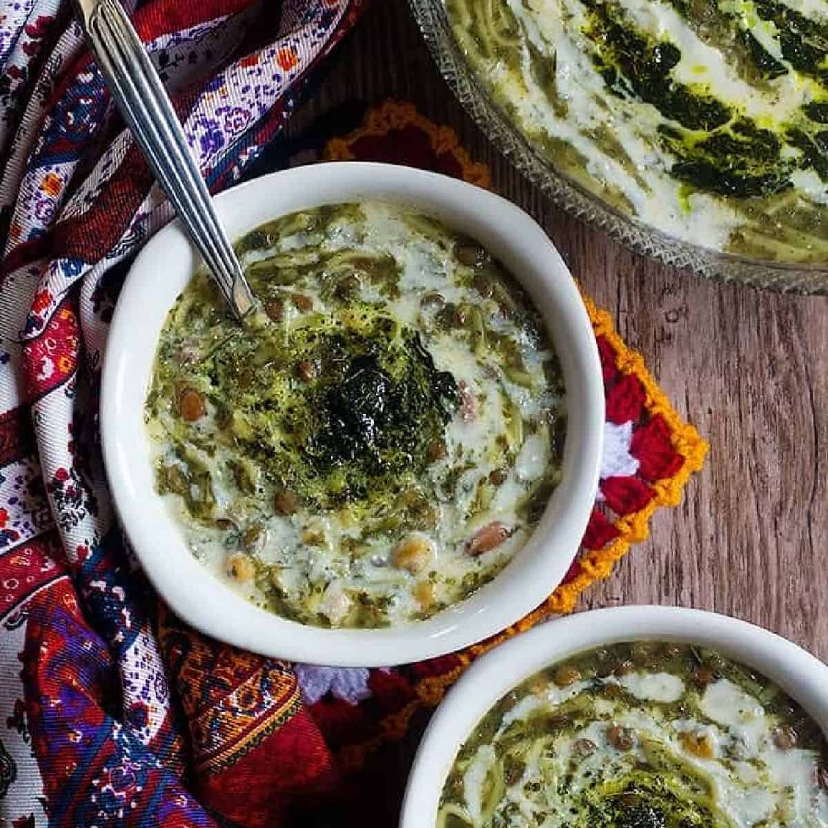 two bowls of Persian noodle soup on a wooden backdrop. 