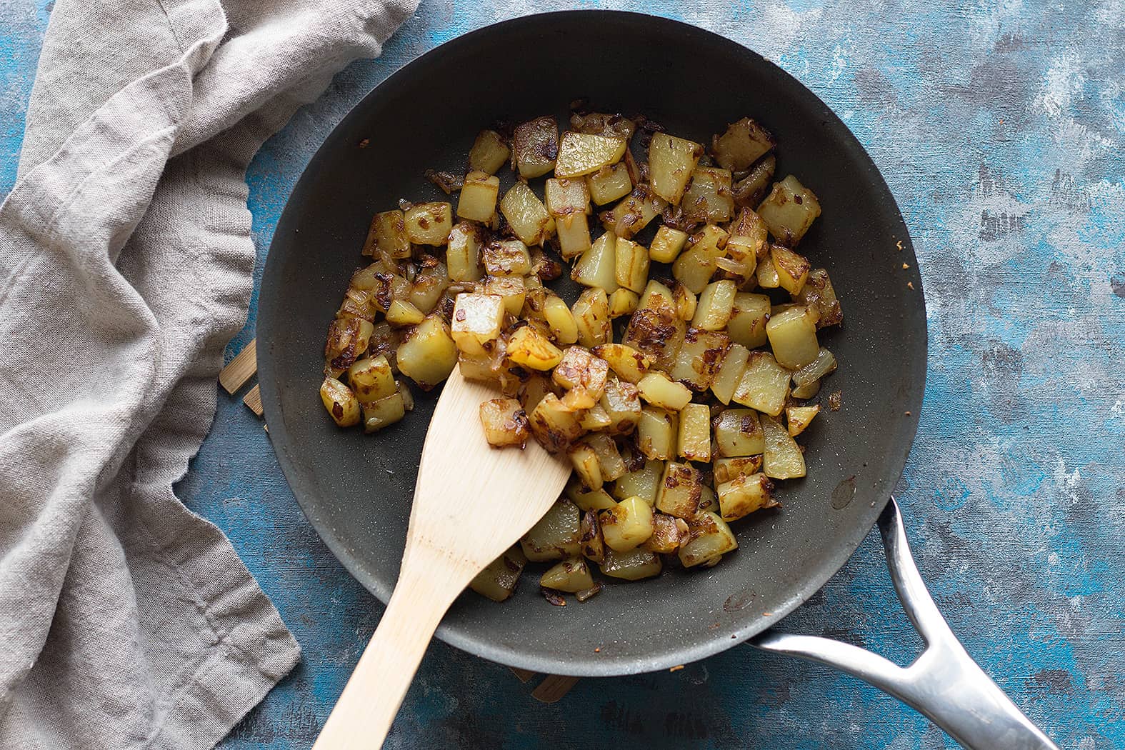 saute potatoes and onions in a pan to make breakfast bowl recipe