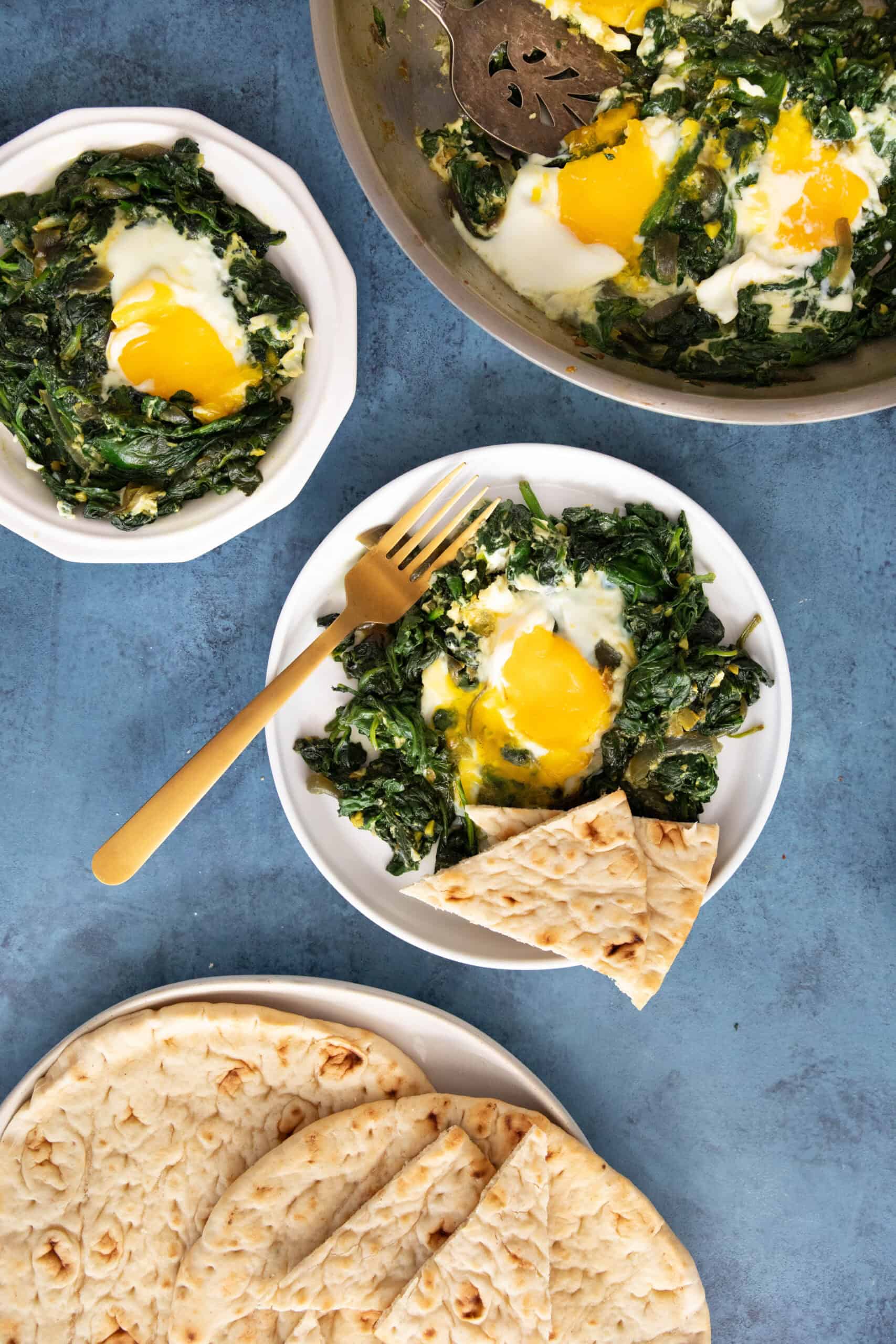 spinach and eggs on 2 plates on a blue backdrop.
