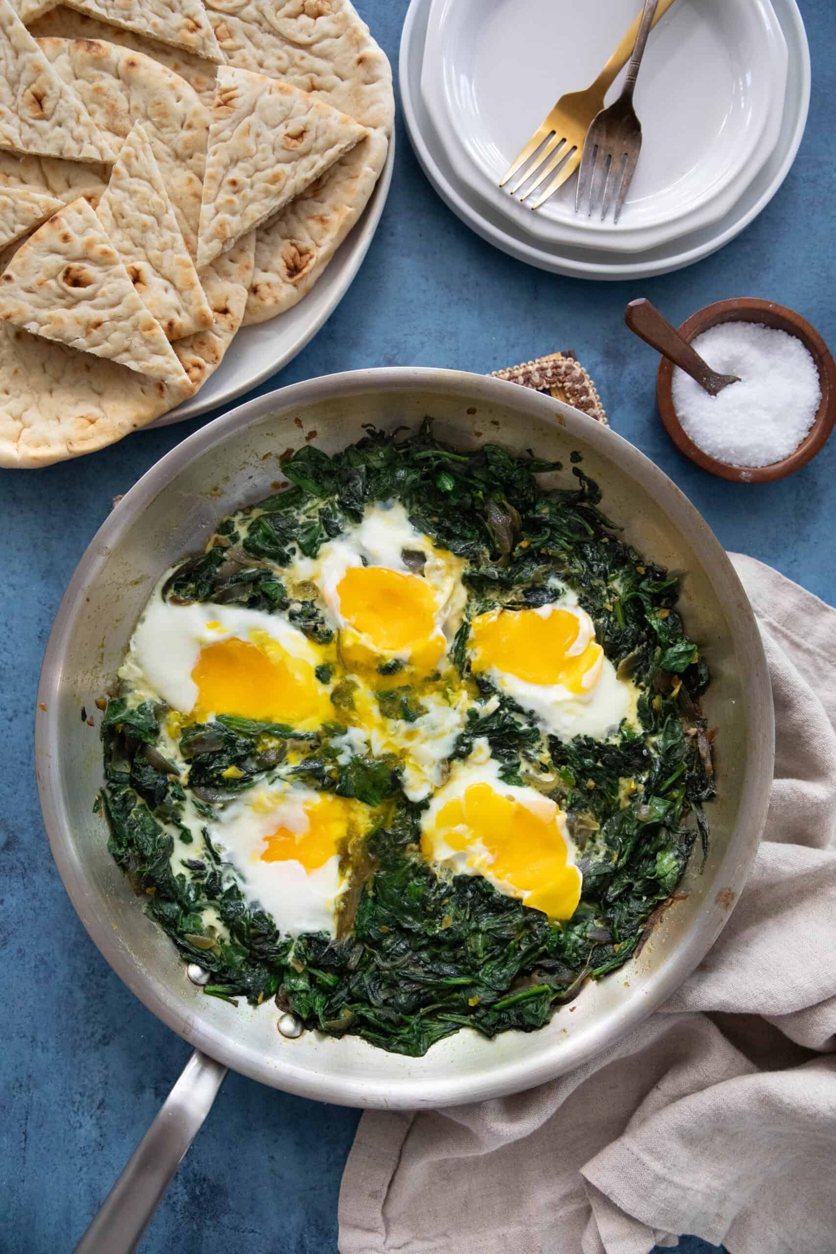 spinach and eggs in a pan on a blue backdrop.