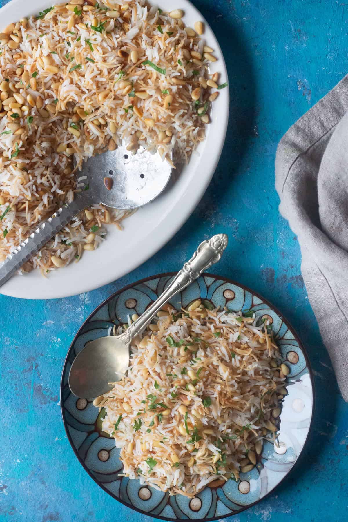 Lebanese pilaf made with rice served on a plate with a spoon and topped with pine nut and parsley.