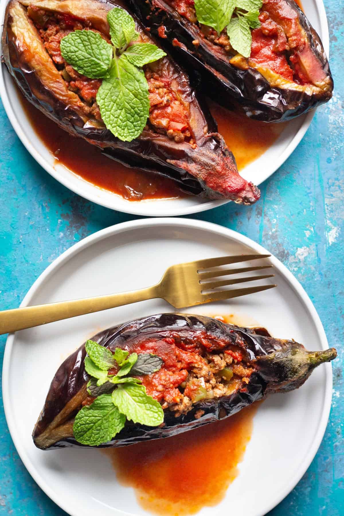 Turkish stuffed eggplant on white plates topped with fresh mint. 
