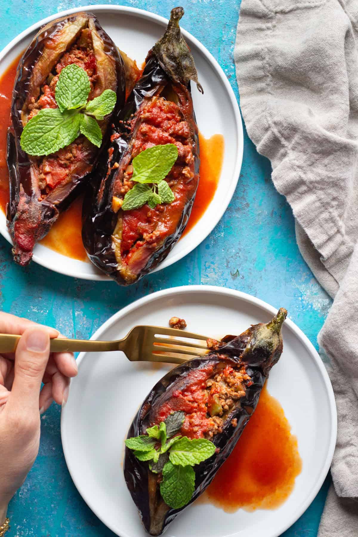 three karniyarik on two different plates with a hand holding a fork.