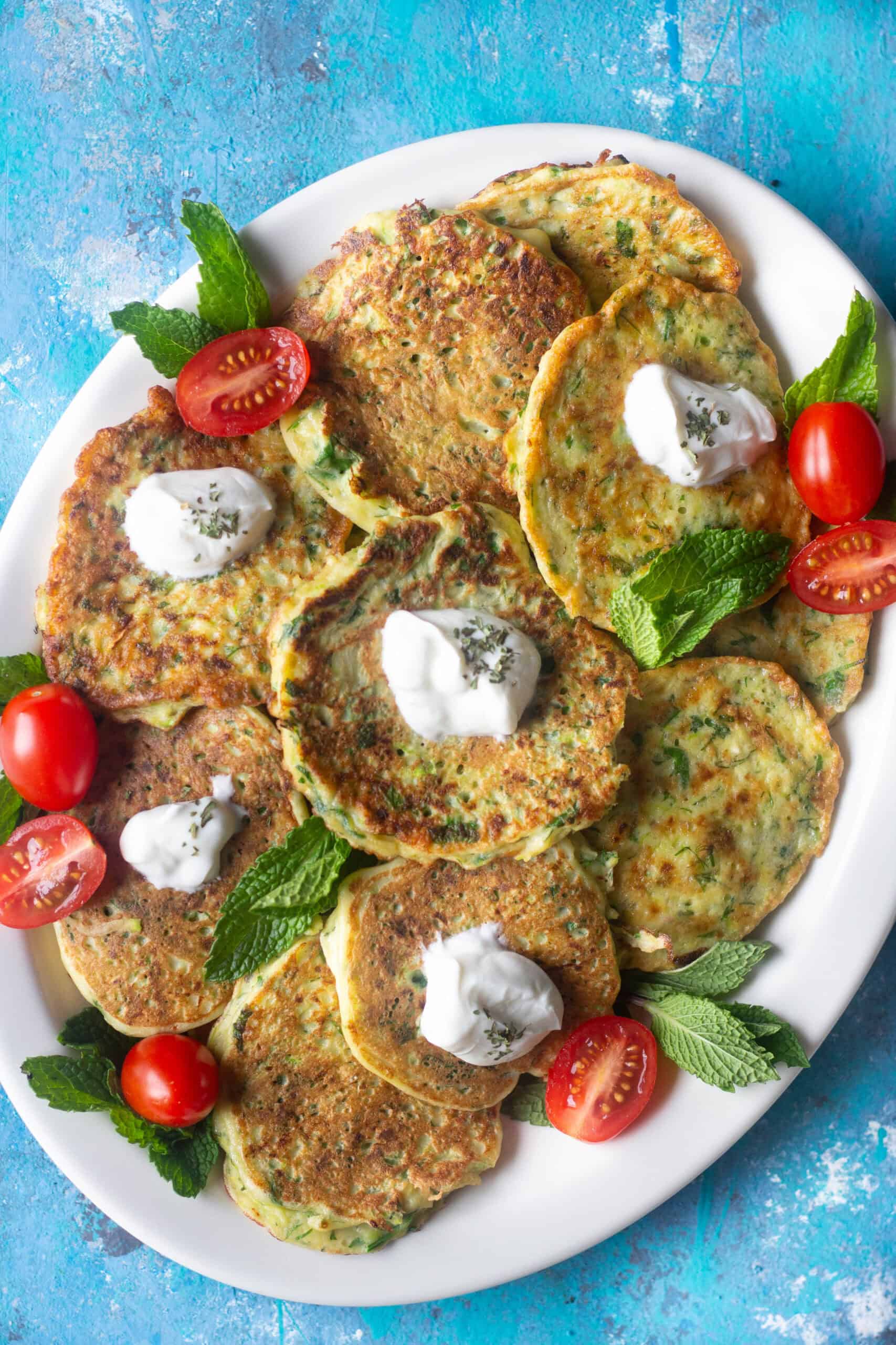 Mücver - Turkish Zucchini Fritters  a top view of a large plate of Turkish zucchini fritters mucver served with a dollop of yogurt and cherry tomatoes