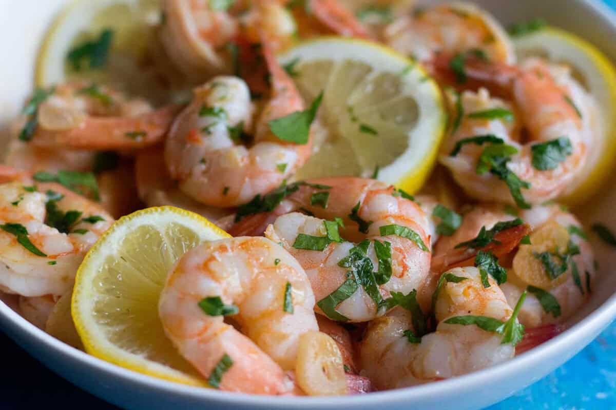 A bowl of sauteed shrimp served with lemon slices. 