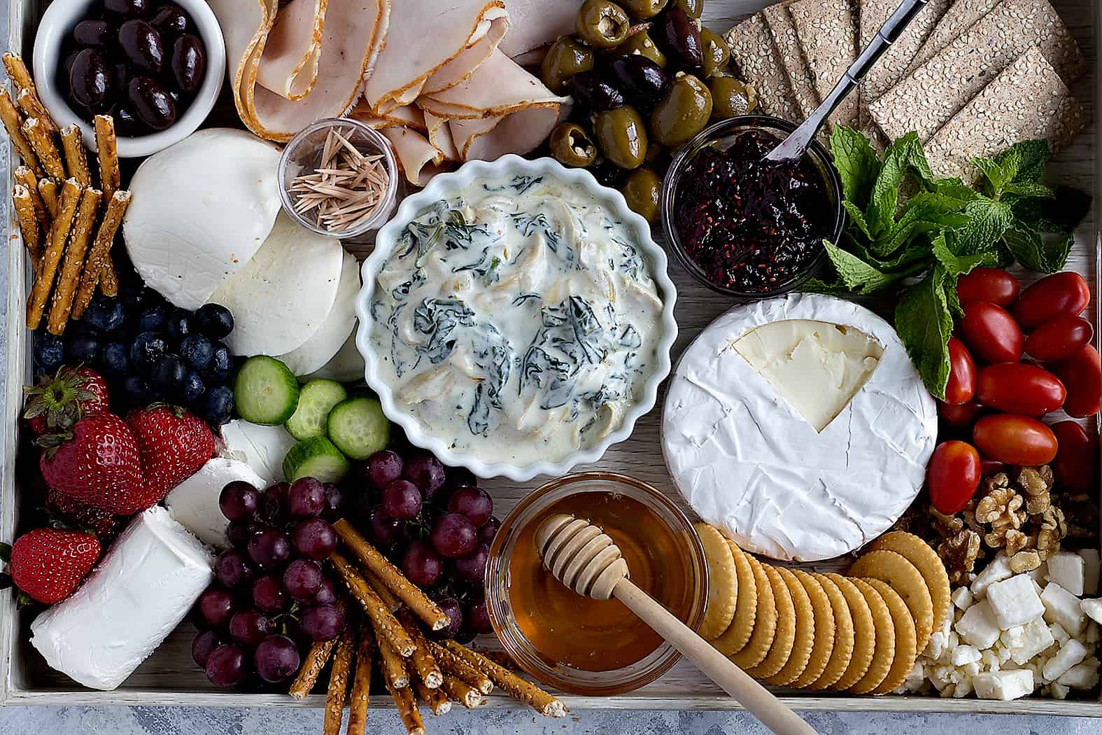 A large and beautiful charcuterie board with cheese, olives, fruit, meat and veggies