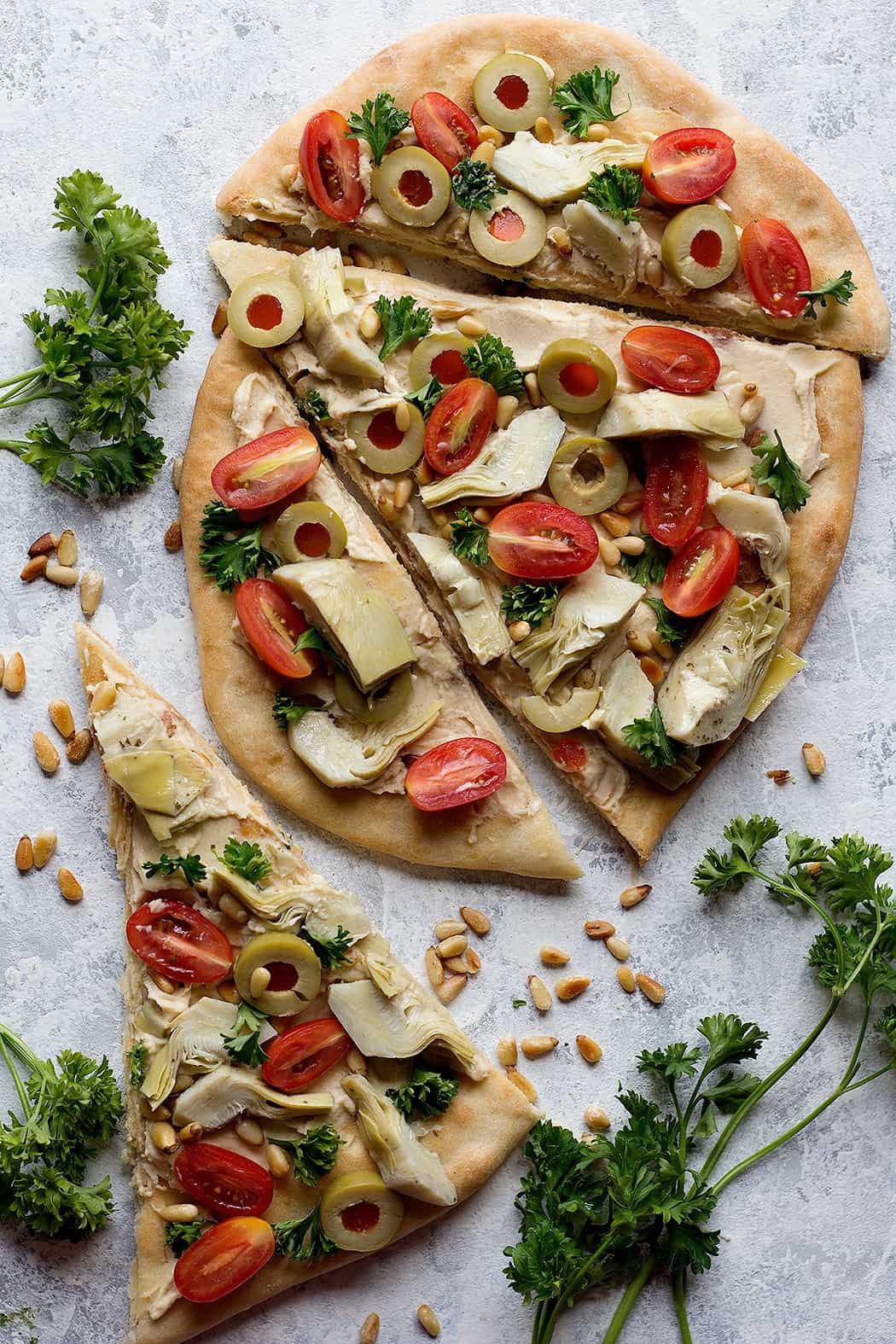 Slices of flatbread topped with hummus, artichoke, tomatoes and pine nuts. 