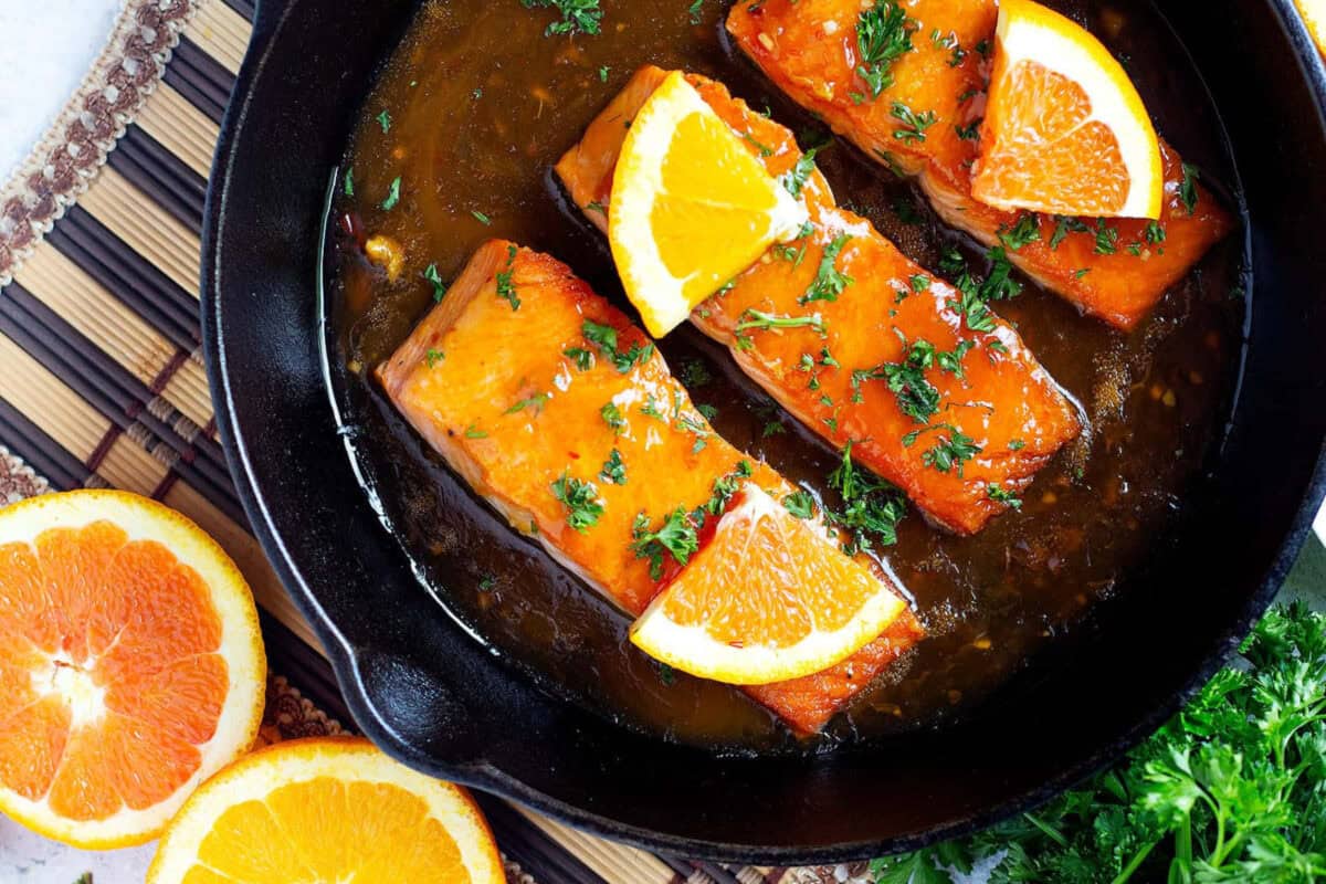 three salmon fillets in a pan with orange sauce.