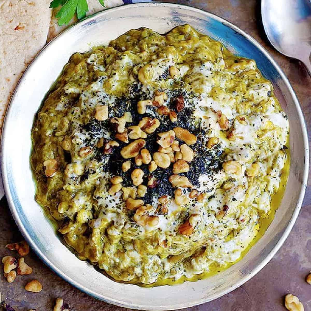 Kashke bademjan on a plate topped with dried mint and walnuts. 