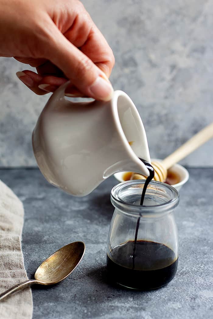 A small creamer of balsamic glaze pouring into a glass jar.