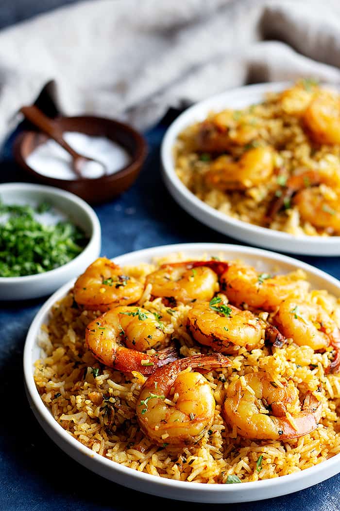 two shrimp and rice dishes on a blue surface with salt and cilantro and a napkin. 