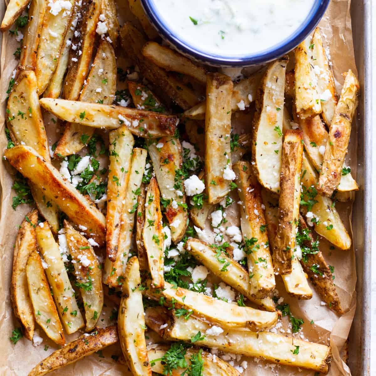 These oven baked fries are crispy on the outside and tender on the inside. They're topped with feta and served with homemade tzatziki.