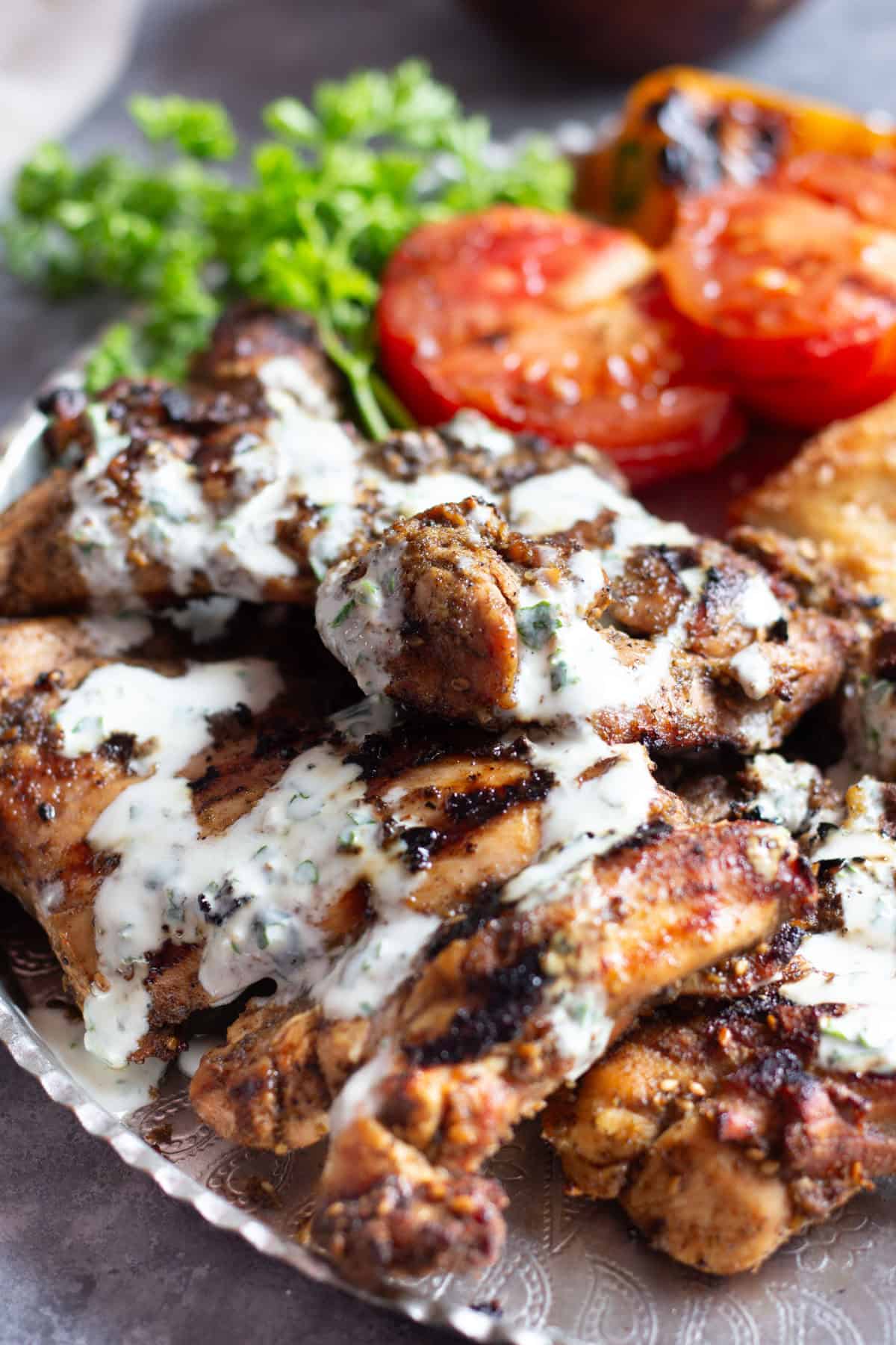 Zaatar chicken served with yogurt sauce on a platter with grilled tomatoes.