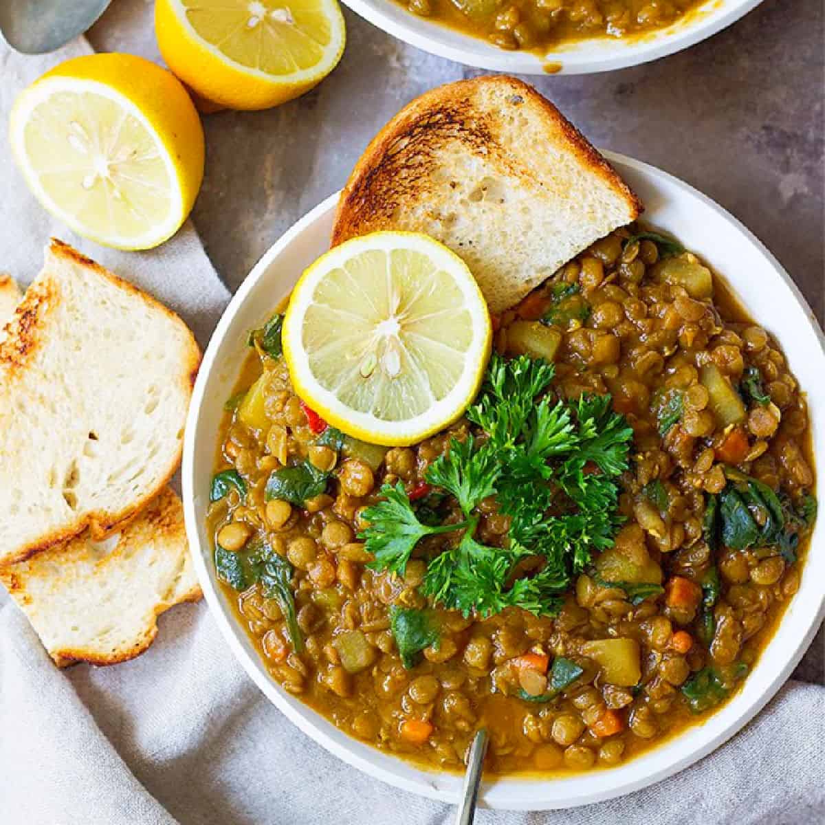 A bowl of Mediterranean green lentil soup topped with parsley and lemon.