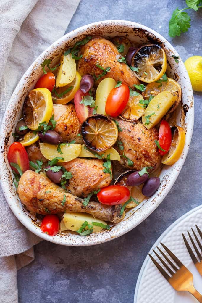 Greek Chicken and potatoes in a baking dish topped with tomatoes and olives. 