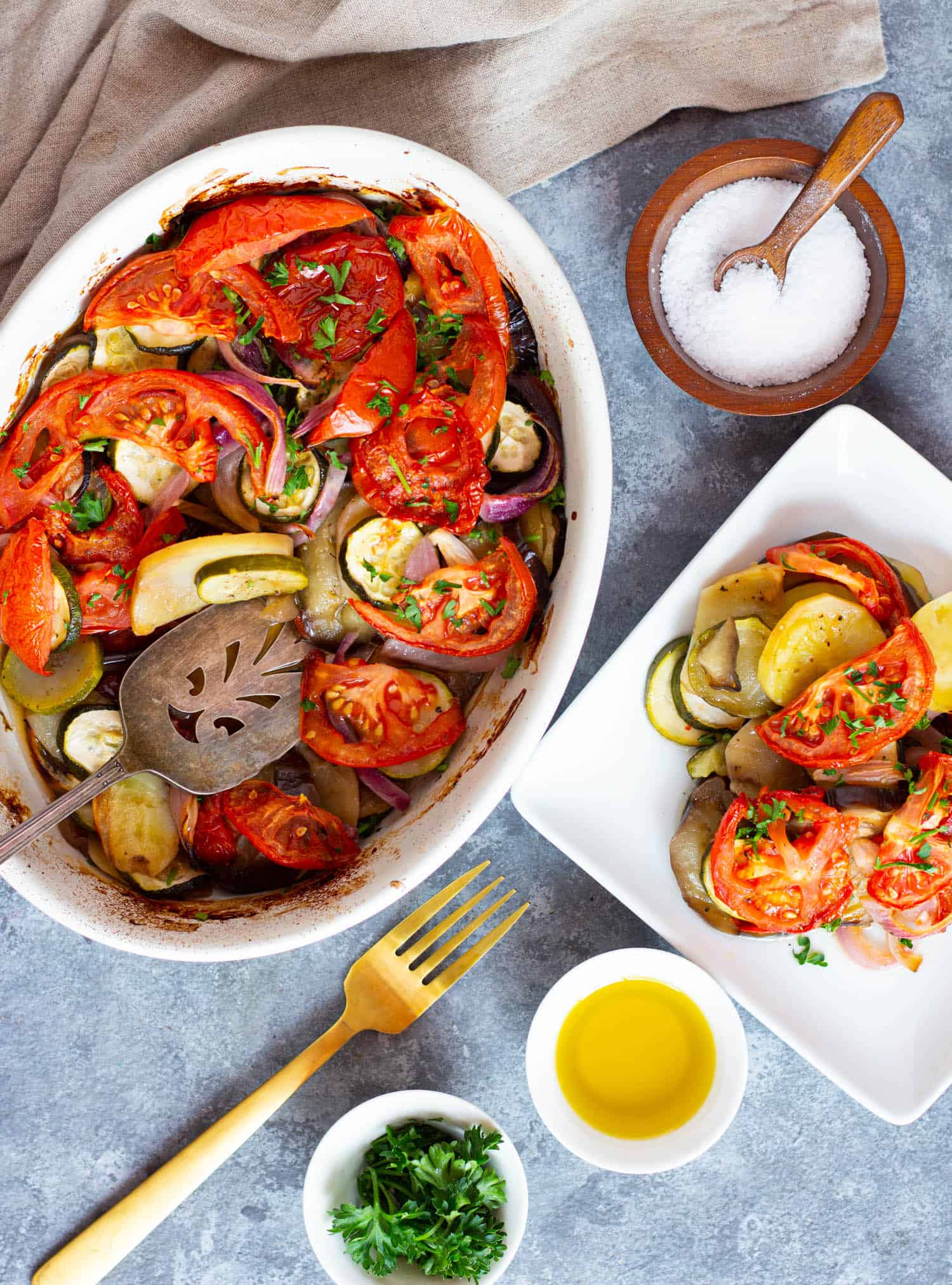 A dish of Greek roasted vegetables and a serving plate filled with vegetables.