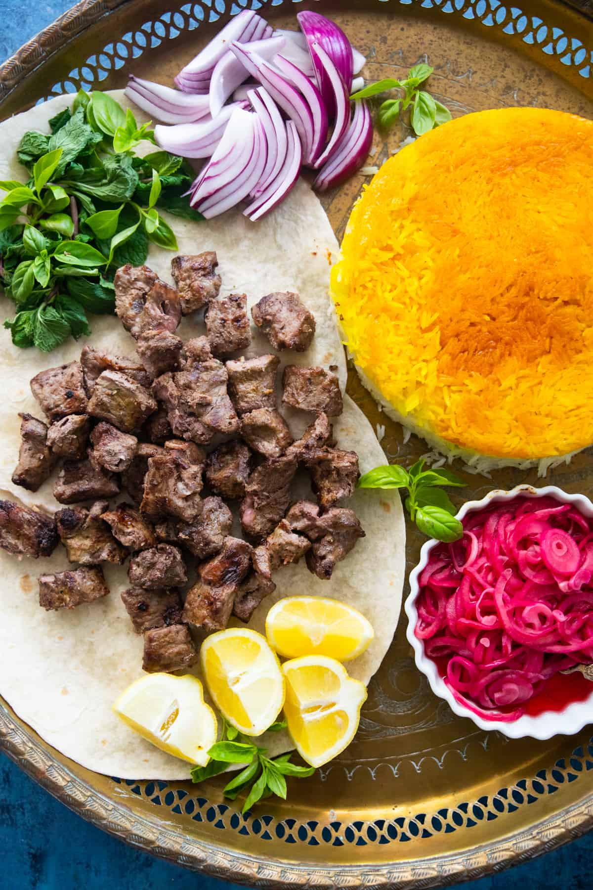 Overhead shot of chenjeh on a platter with onions an saffron rice. 