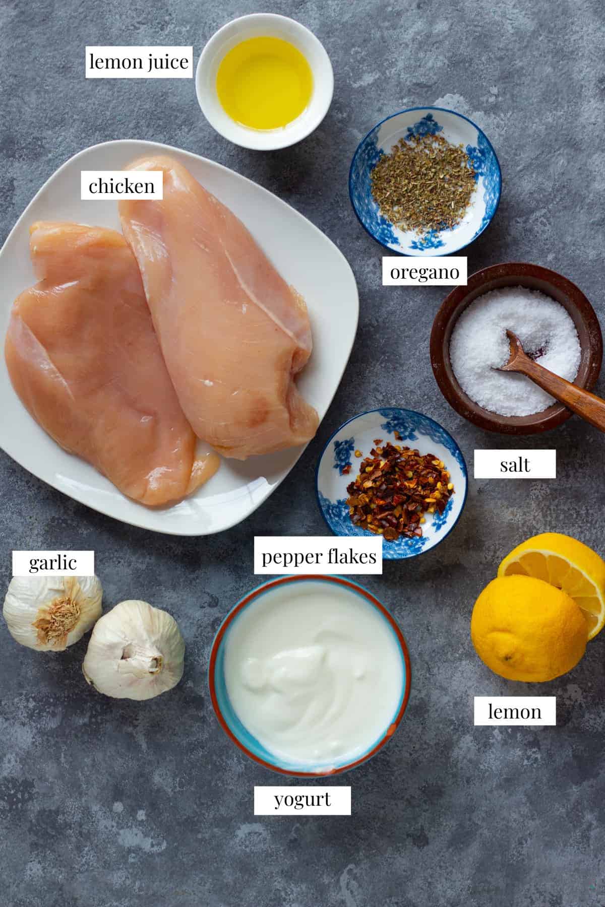 Ingredient shot for the recipe including olive oil, oregano, chicken, pepper, salt and lemon. 