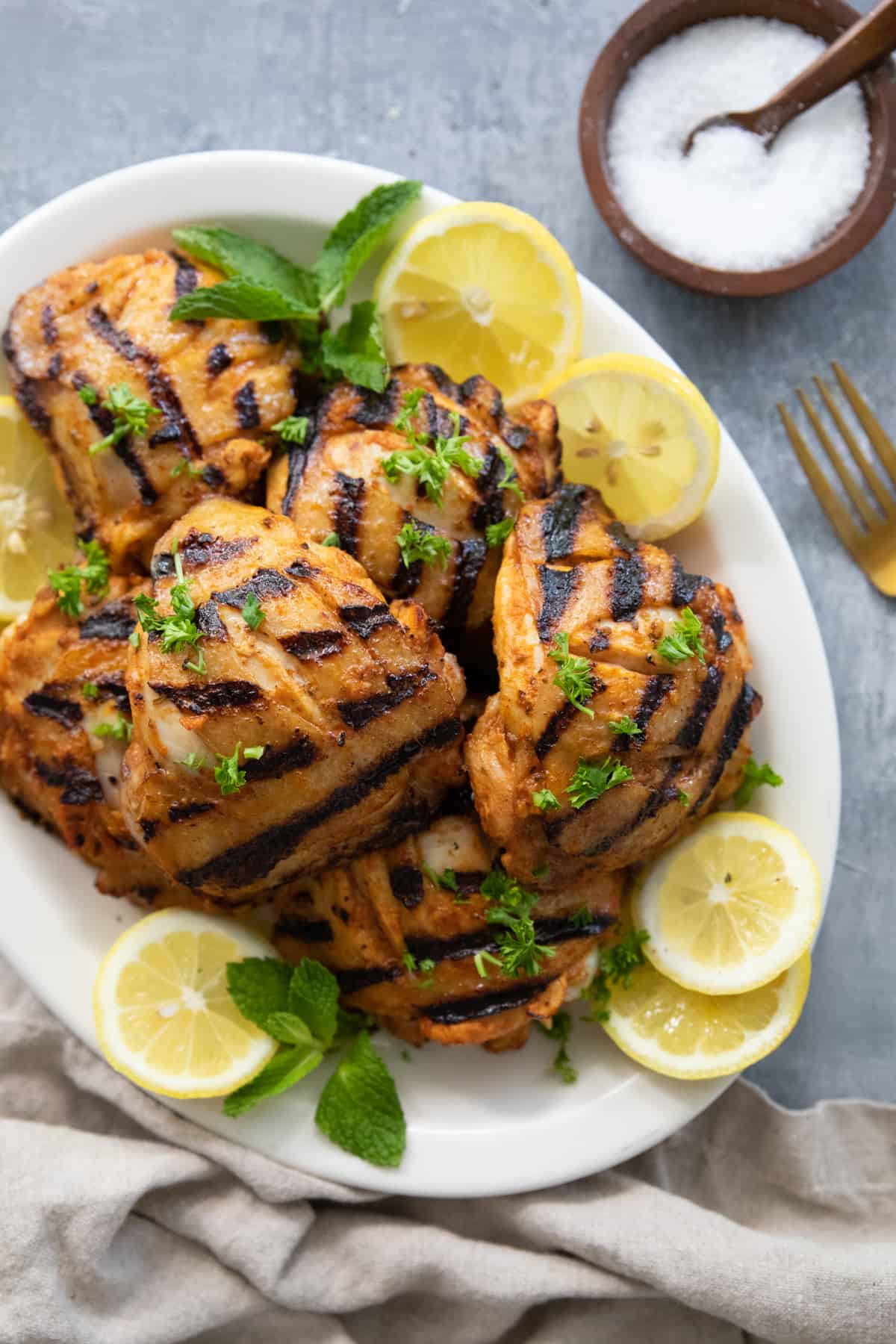 Grilled chicken thighs with harissa and garlic in a white plate with lemon slices. 