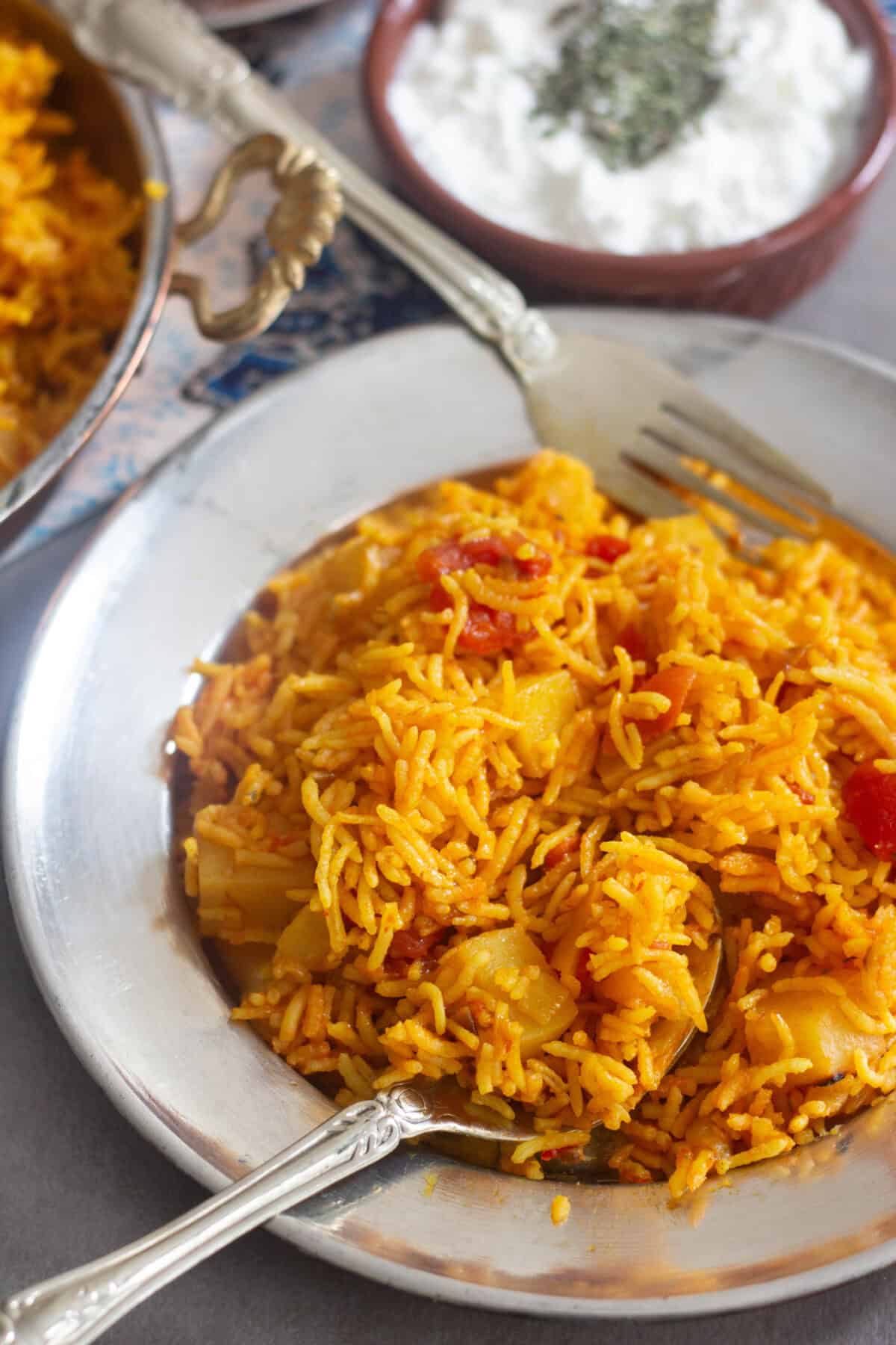 A plate of Persian style tomato rice with yogurt on the side. 