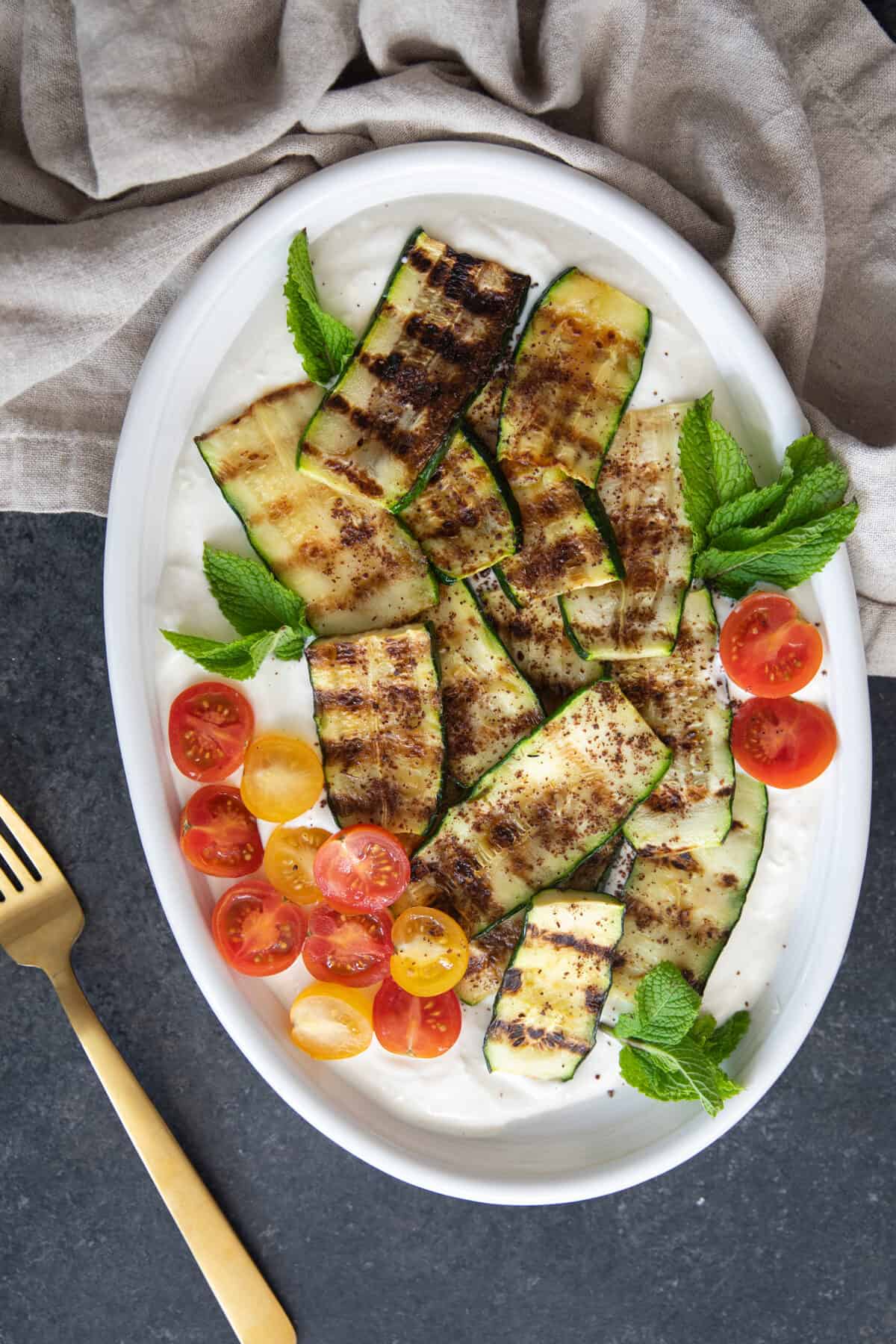 Overhead shot of grilled zucchini on tahini yogurt sauce in a platter. 