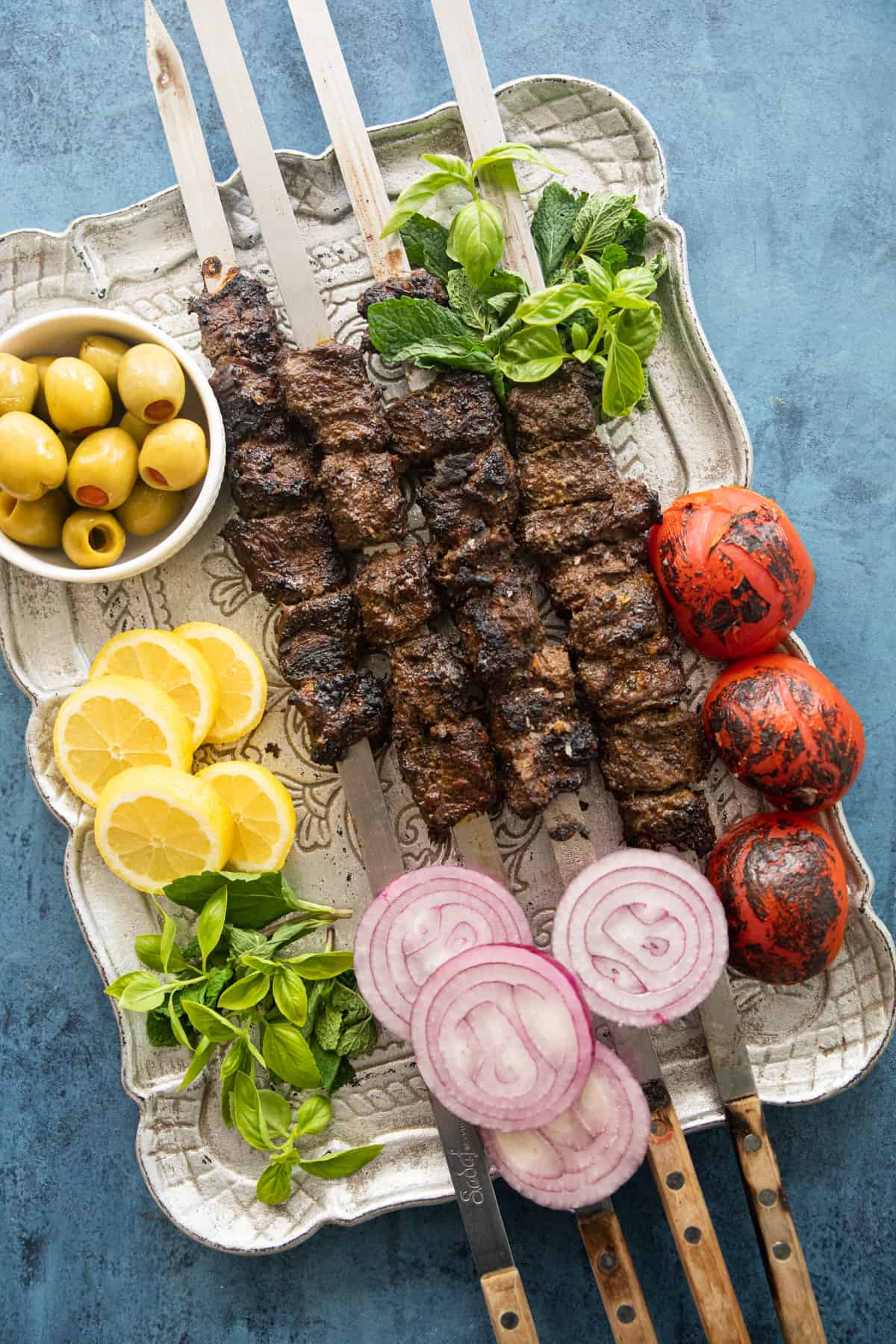 Kabob torsh skewers on a platter with olives, lemon and tomatoes. 