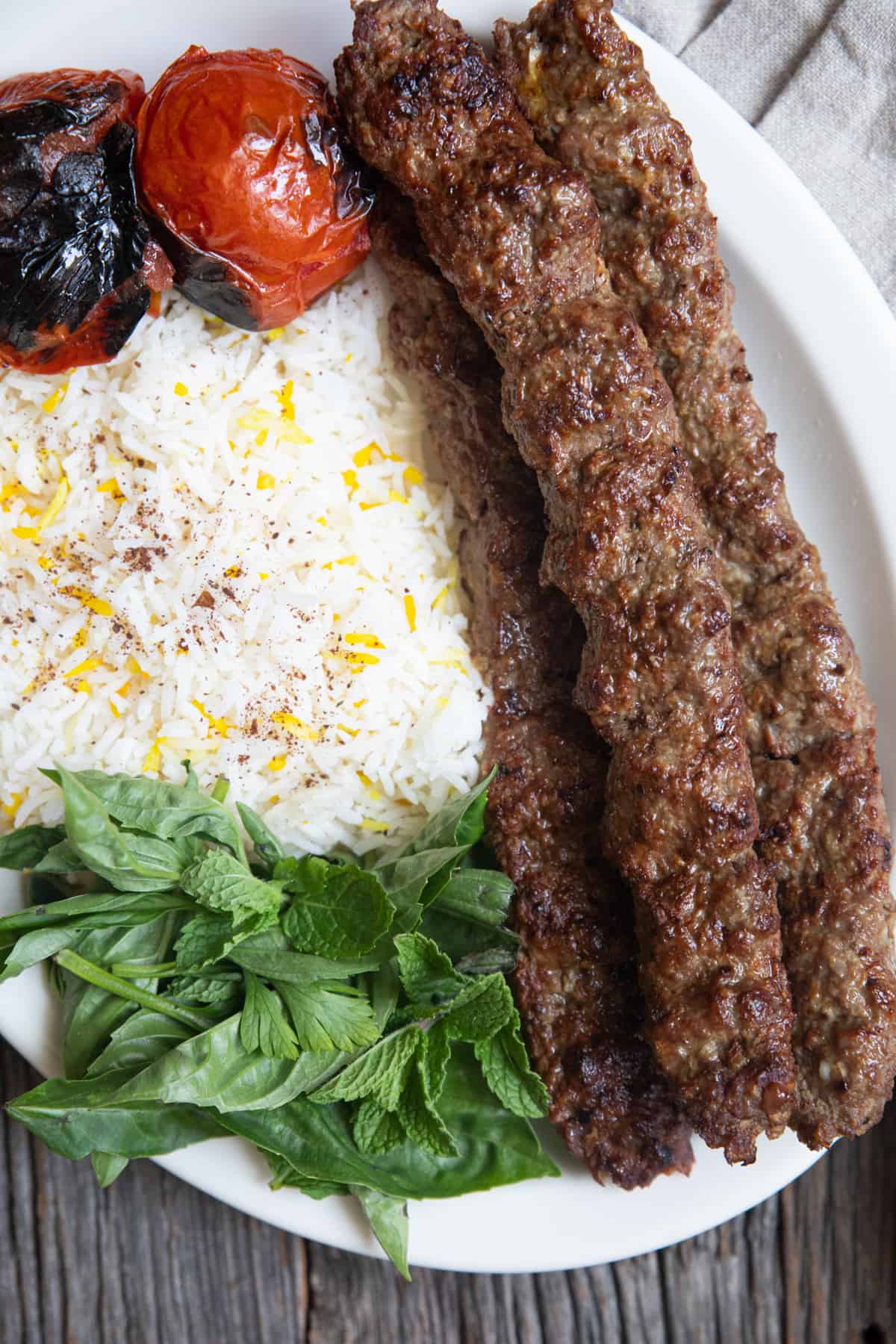 kabab koobideh on a plate with rice and tomatoes. 