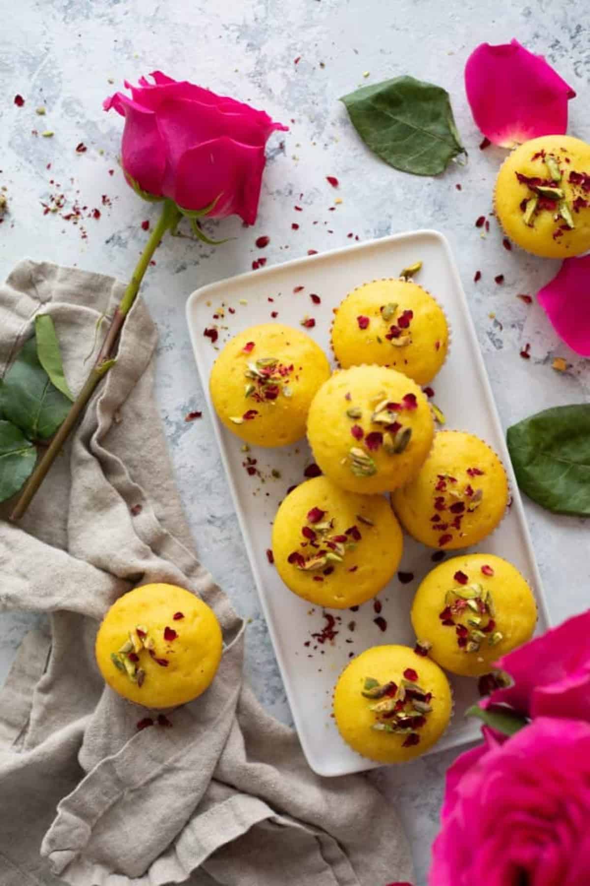 Overhead shot of saffron muffins with pink roses on a white background.