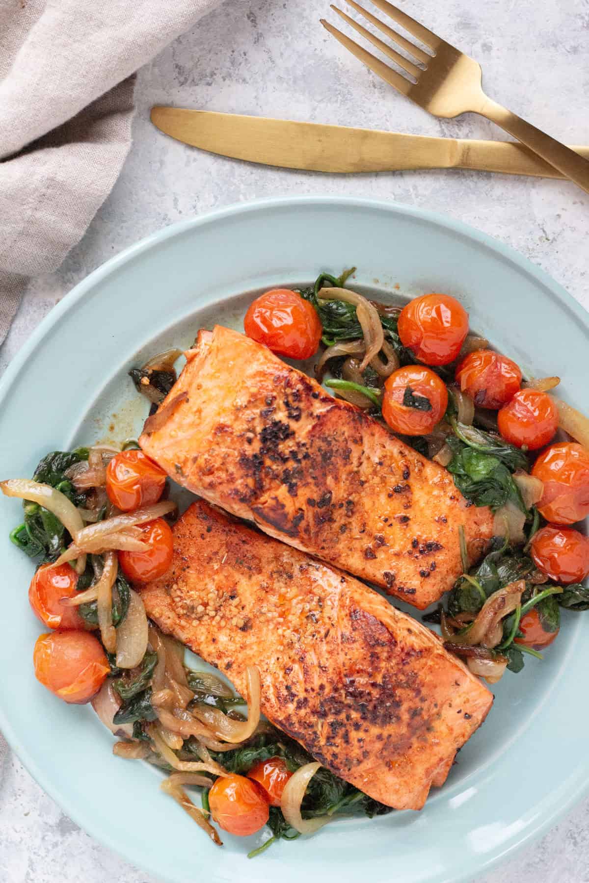 overhead shot of two salmon fillets with tomatoes and spinach. 