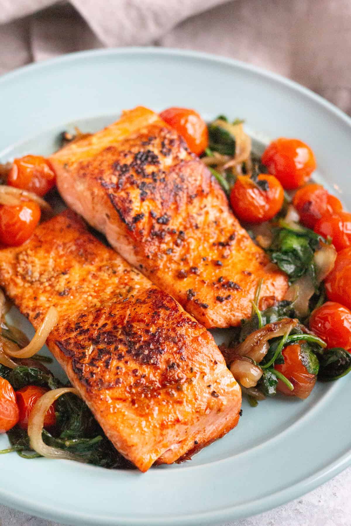 pan seared salmon fillets on a plate with cooked spinach and tomatoes. 
