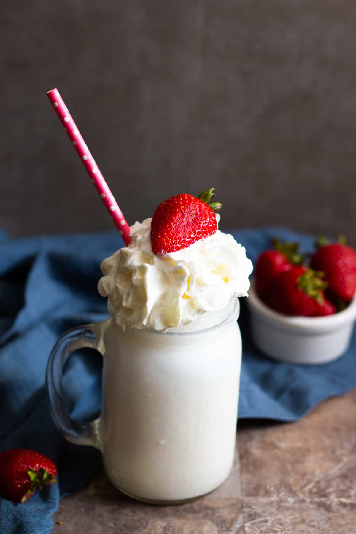 how to make a milkshake - A glass of vanilla milkshake topped with strawberries and whipped cream.