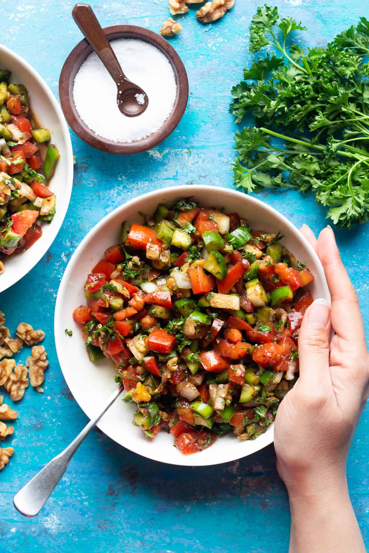 A bowl of tomato salad Turkish style with a bunch of parsley and salt on a blue background.