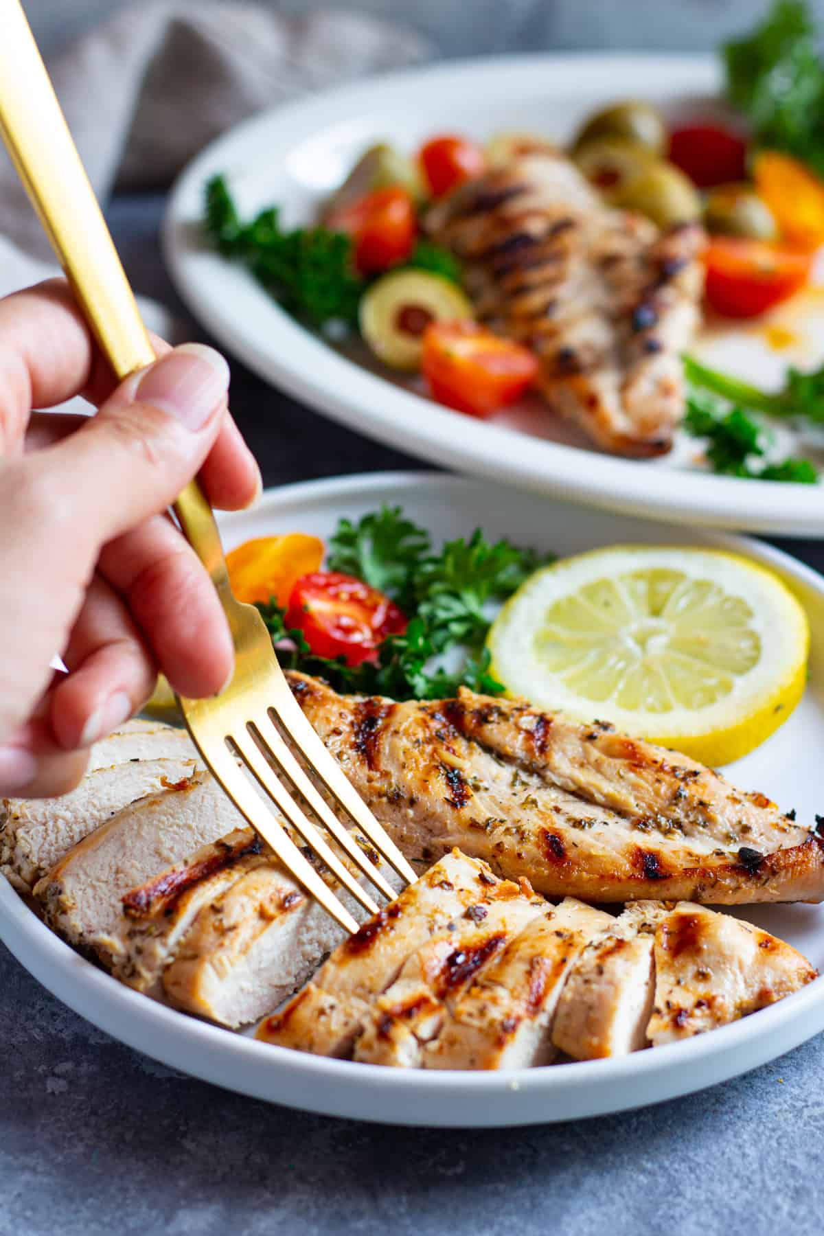 Greek grilled chicken sliced and served on a plate with lemon and herbs.