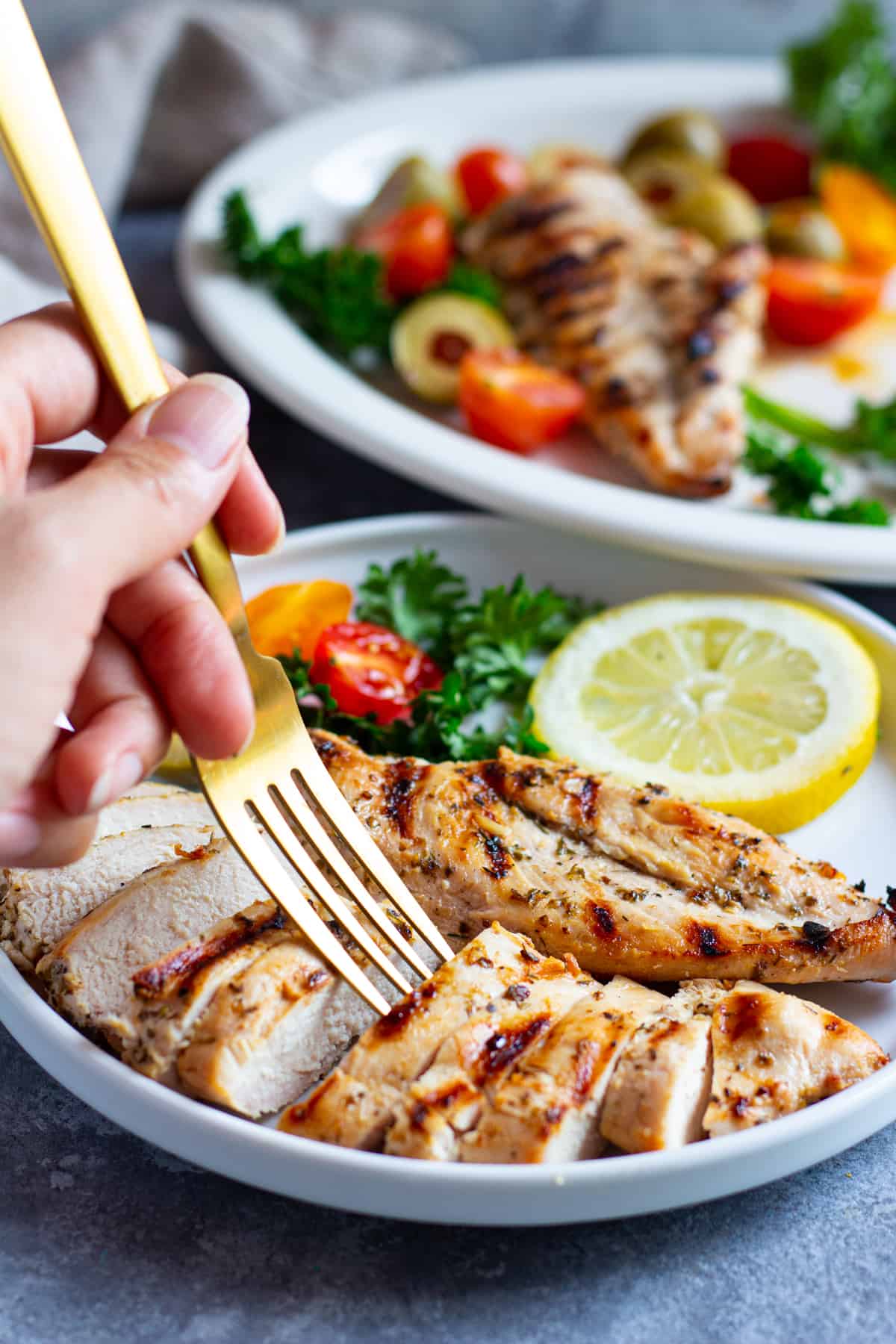 Greek grilled chicken sliced and served on a plate with lemon and herbs. 