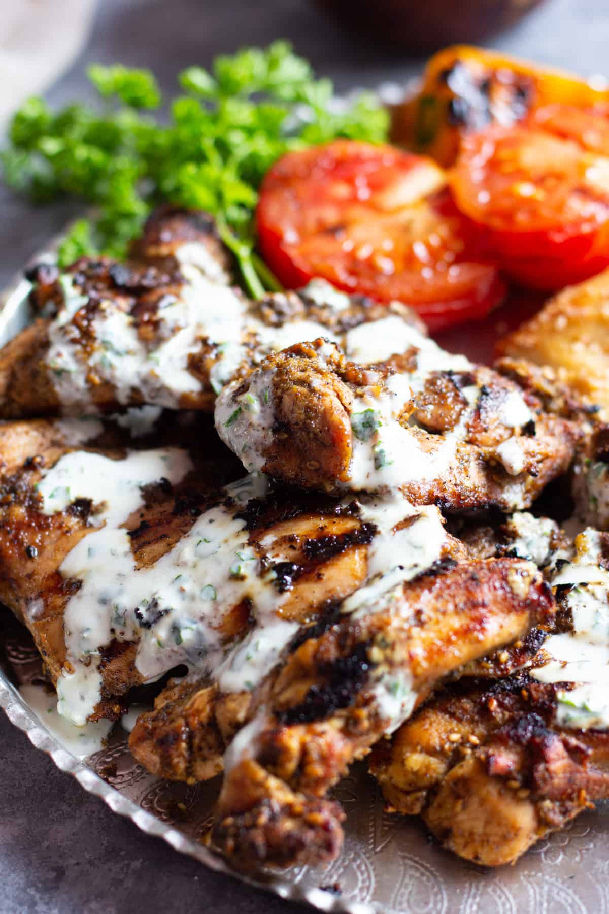 Zaatar chicken served with yogurt sauce on a platter with grilled tomatoes.