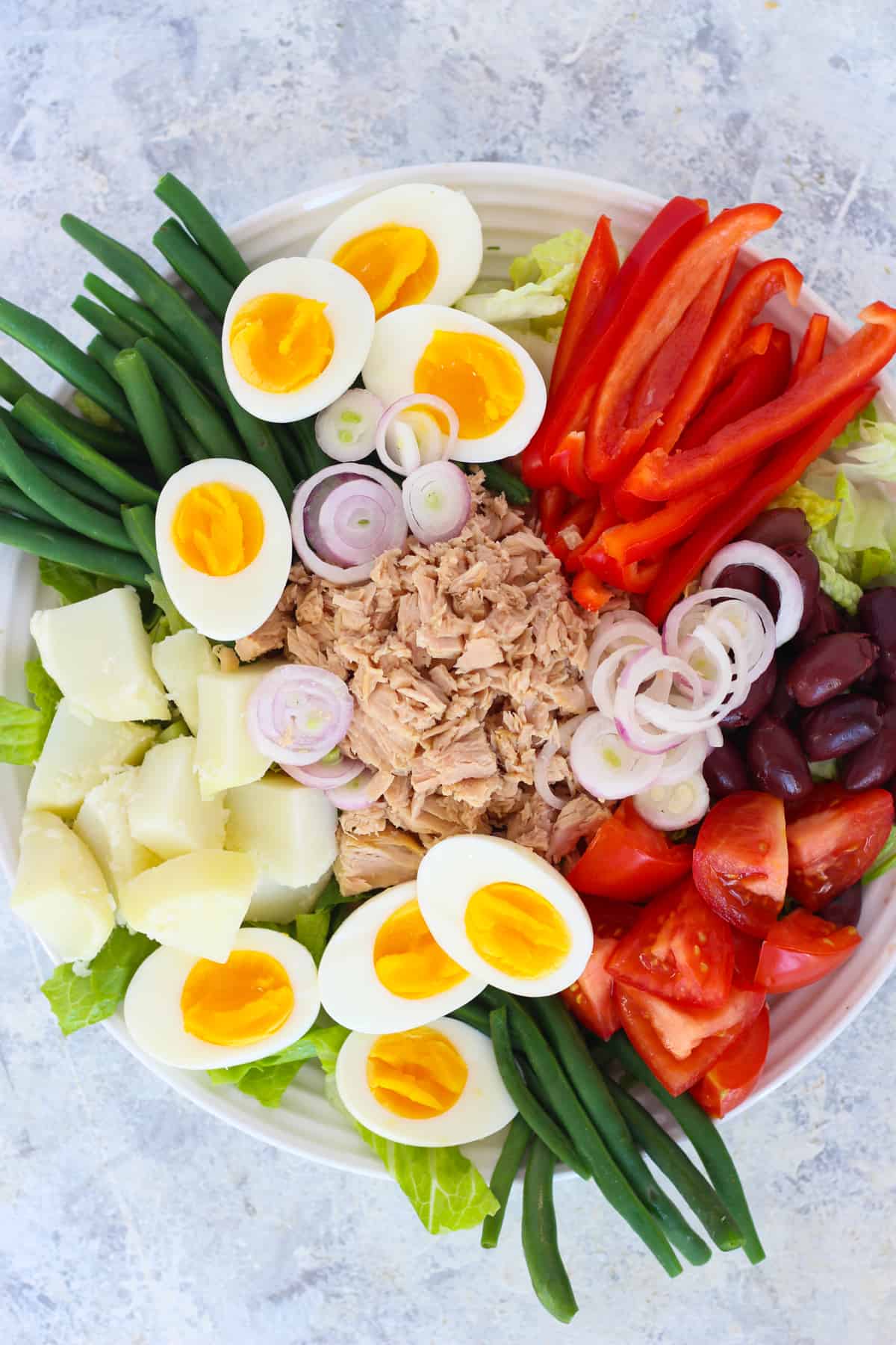 Nicoise salad is a French salad that is composed. The ingredients are arranged beautifully on a bed of lettuce.