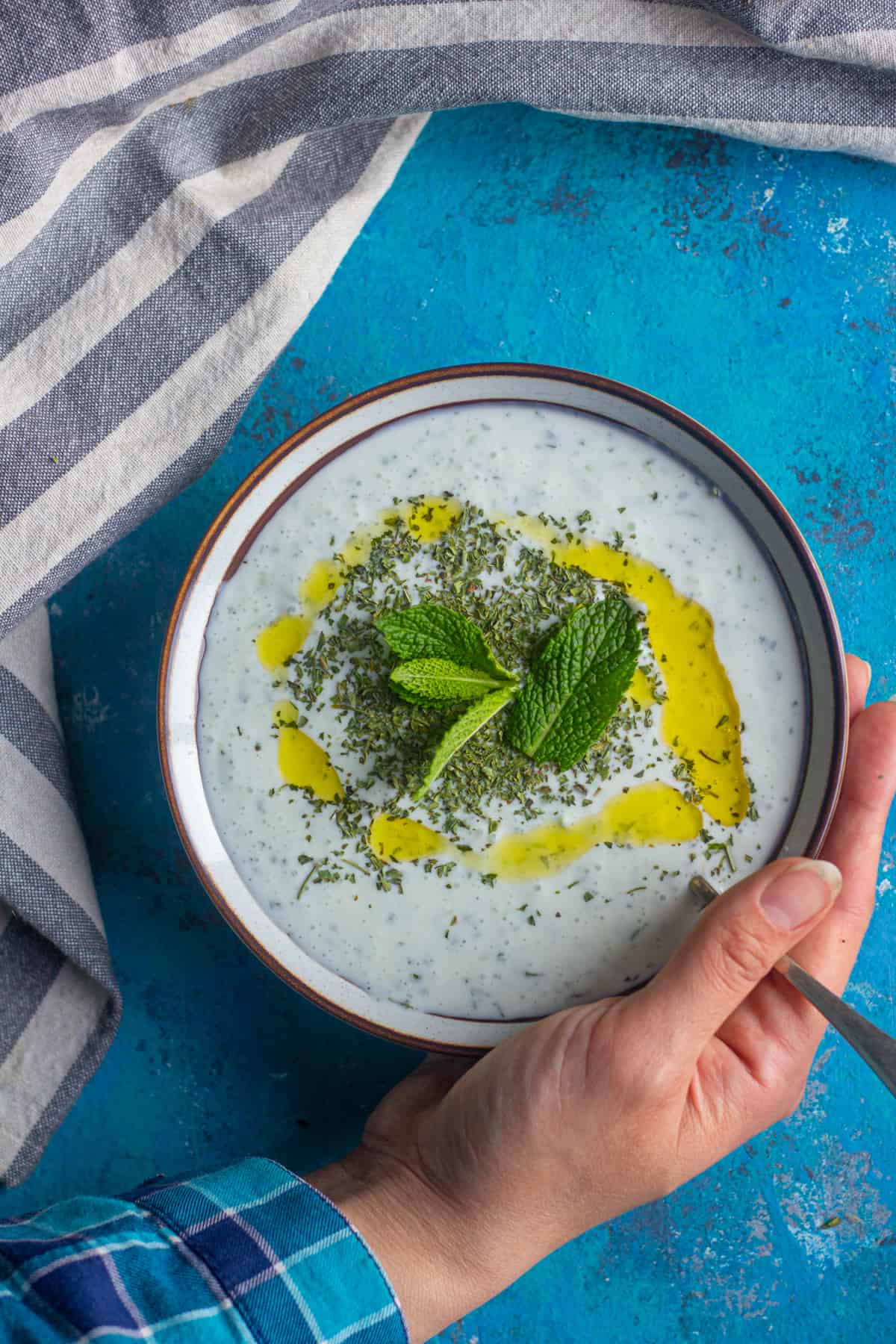 A hand holding a bowl of Turkish appetizer made with yogurt and cucumber